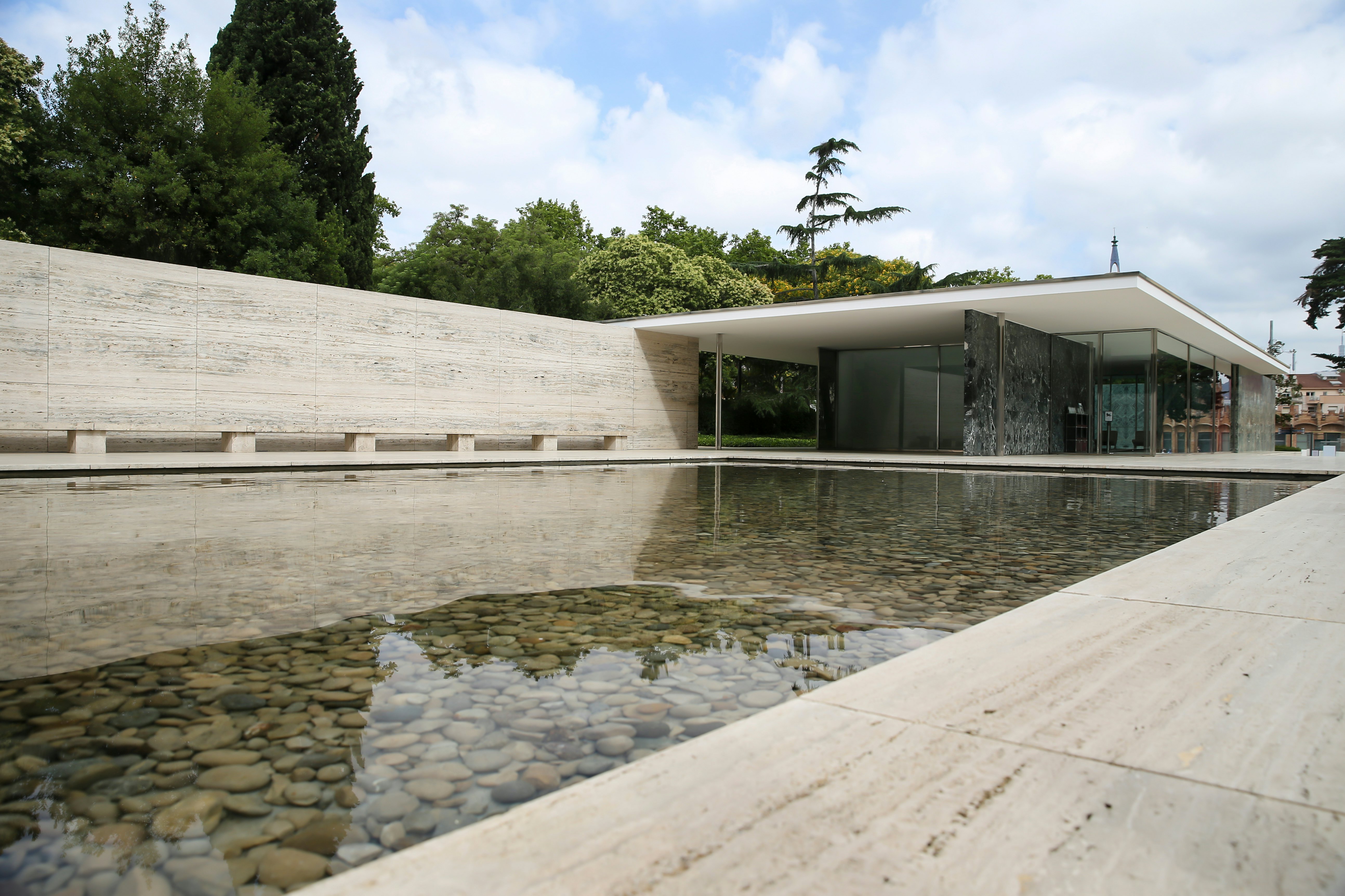 A low pool filled with smooth rocks borders a walkway that leads to a single-story pavilion with a flat roof.