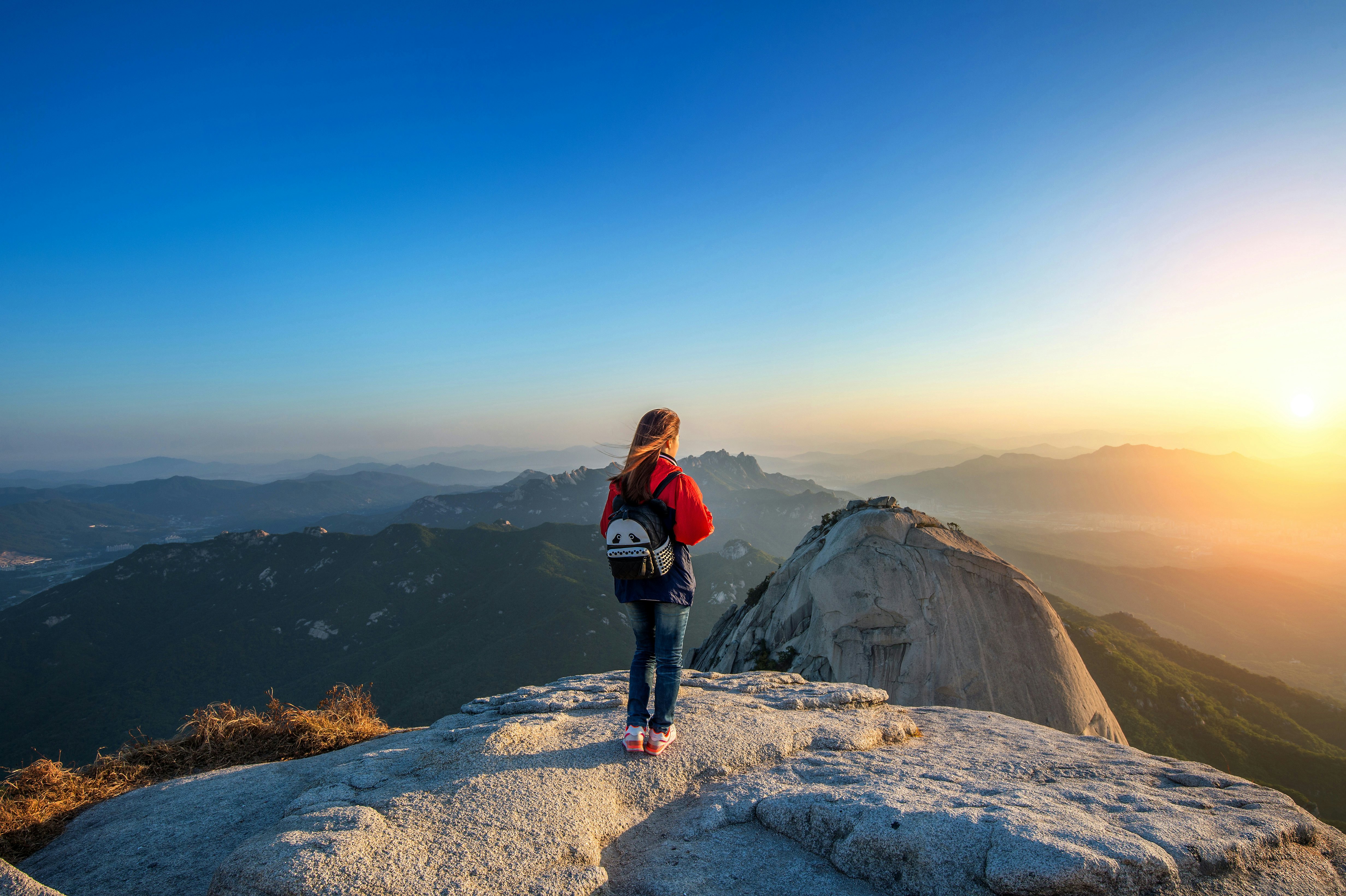 A hiker stands on a rocky outcrop watching the sunrise over mountains in a national park.