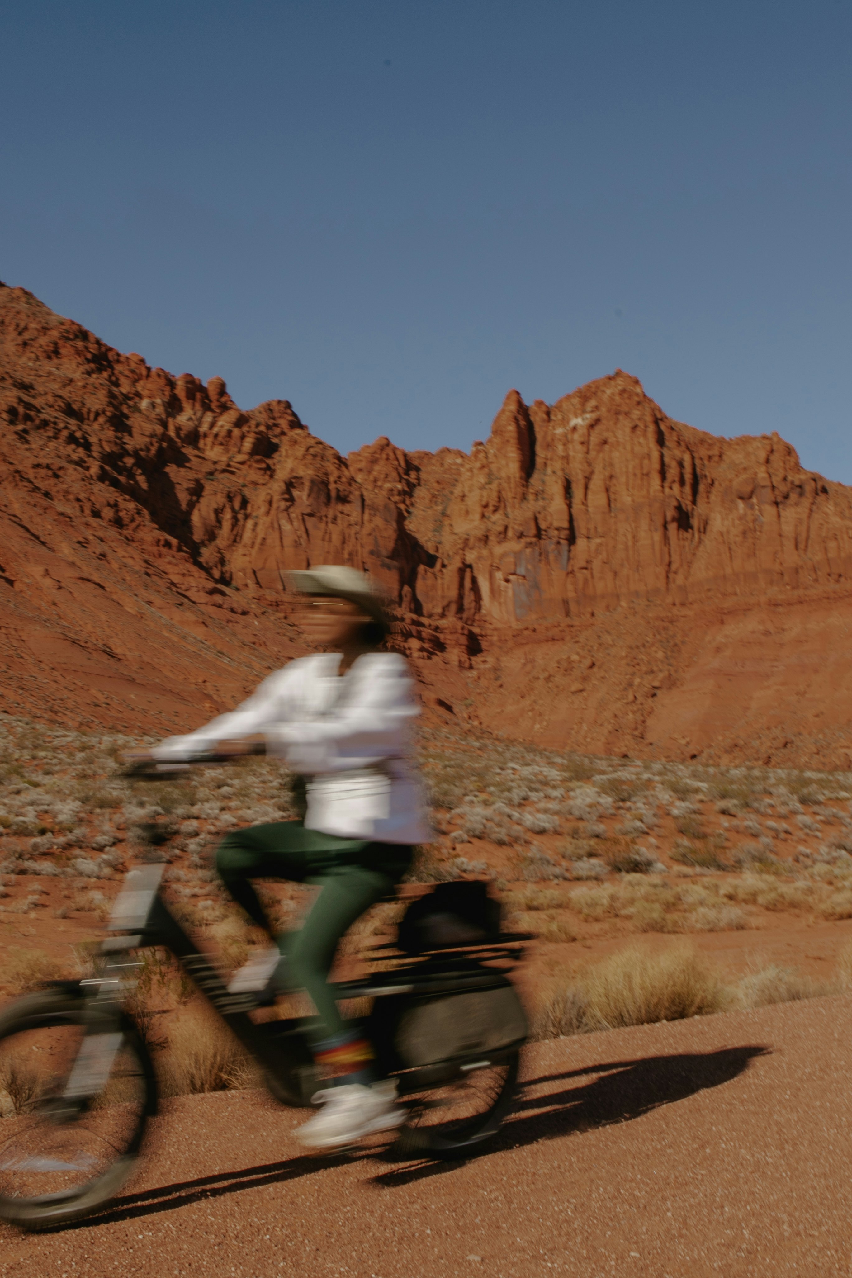 A blurred woman on a bike rides past reddish rock formations.