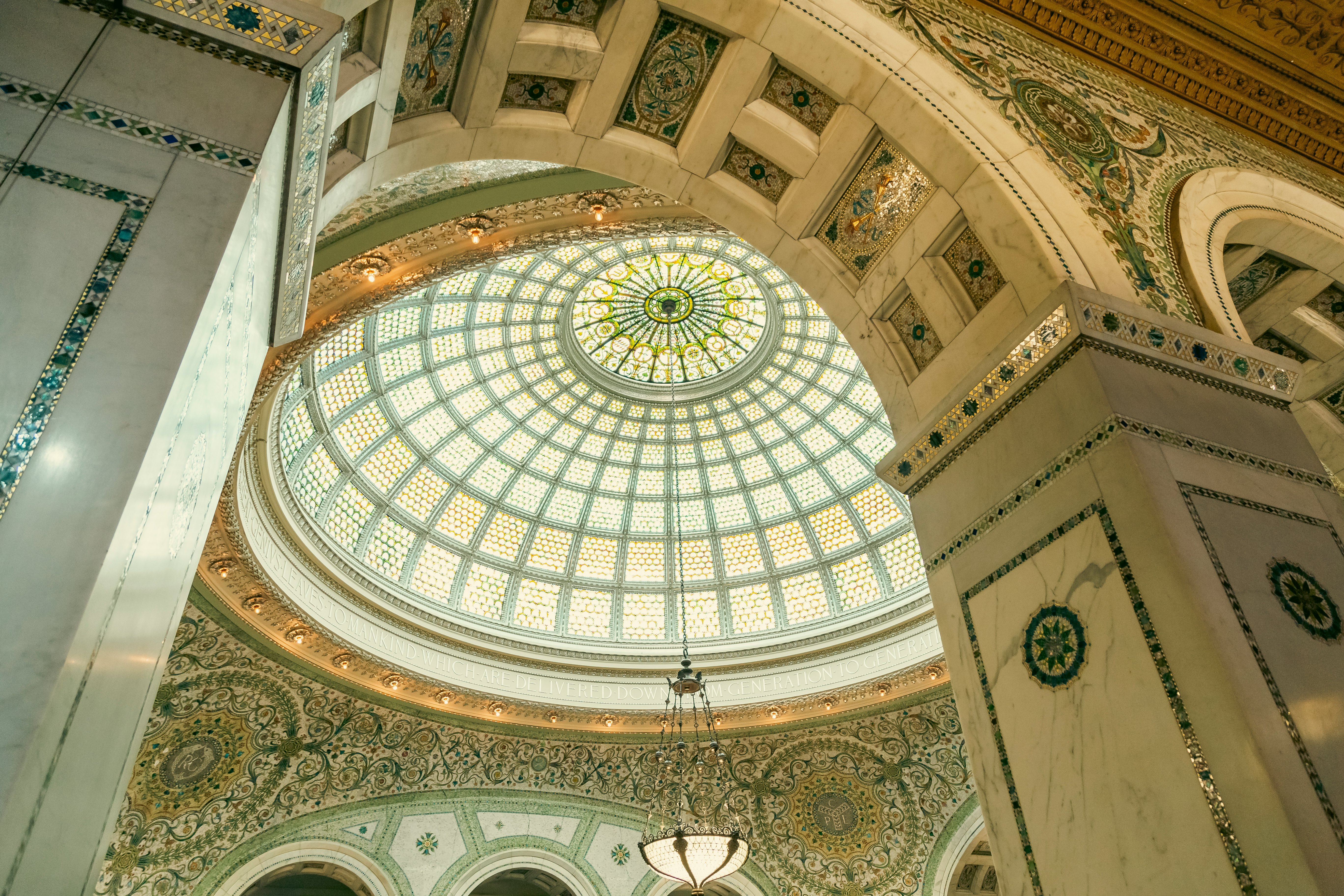 A glass-paneled dome in a rotunda, with a stained glass design at the apex; an elaborately detailed archway is in the foreground, framing the dome.