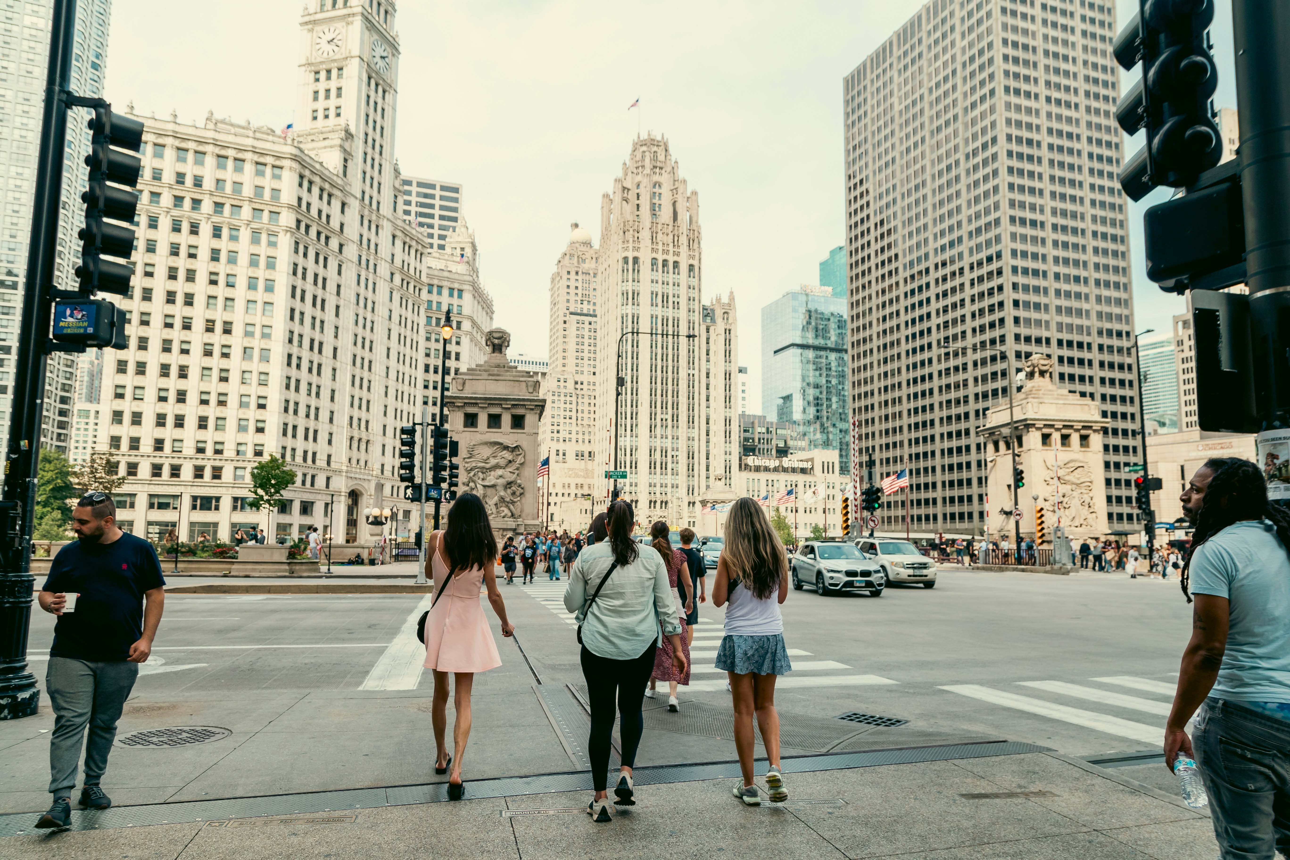 People walk across a crosswalk in the direction of a tall white skyscraper.