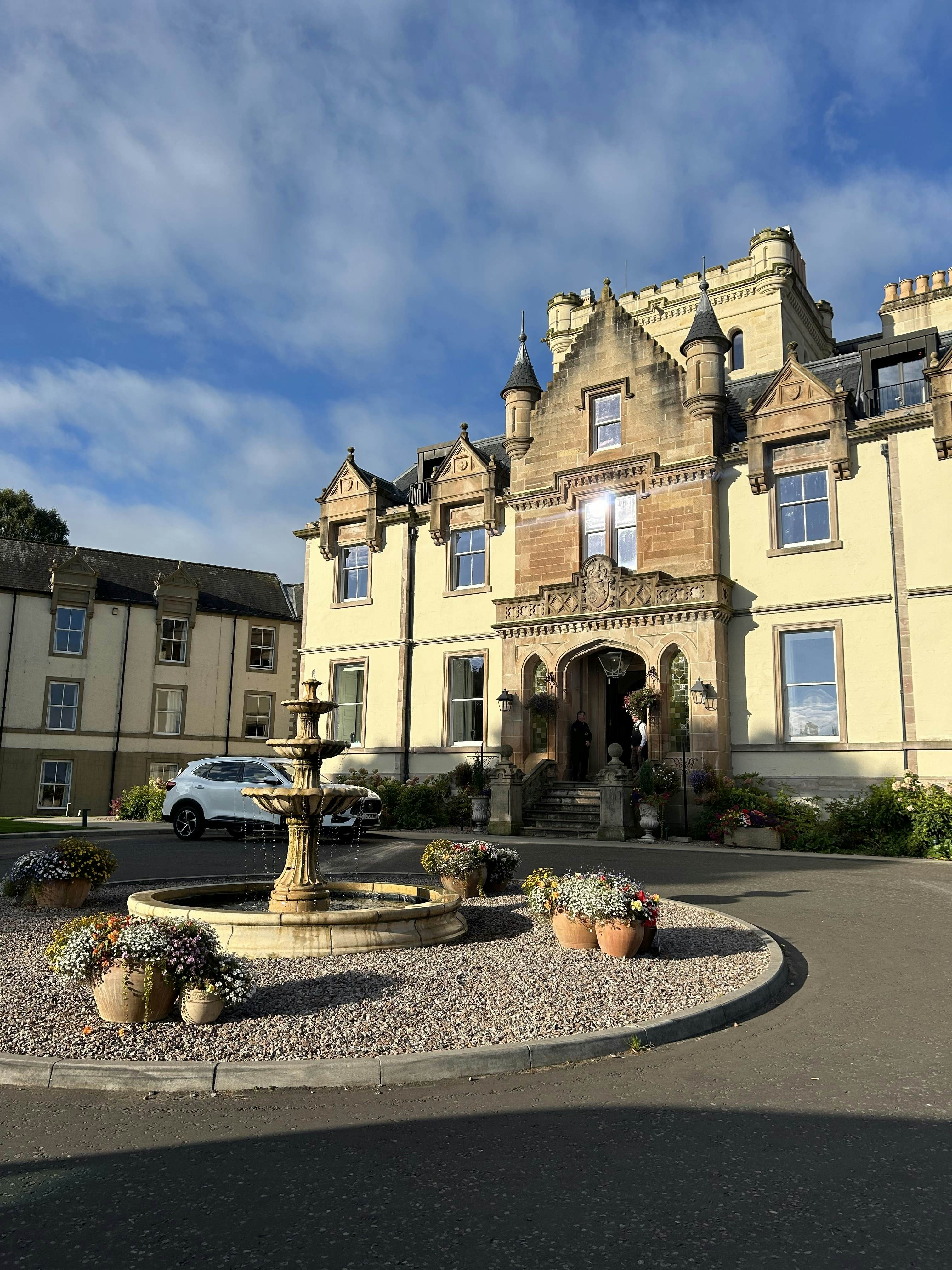 A driveway curves around a fountain in front of a hotel in a historic building.