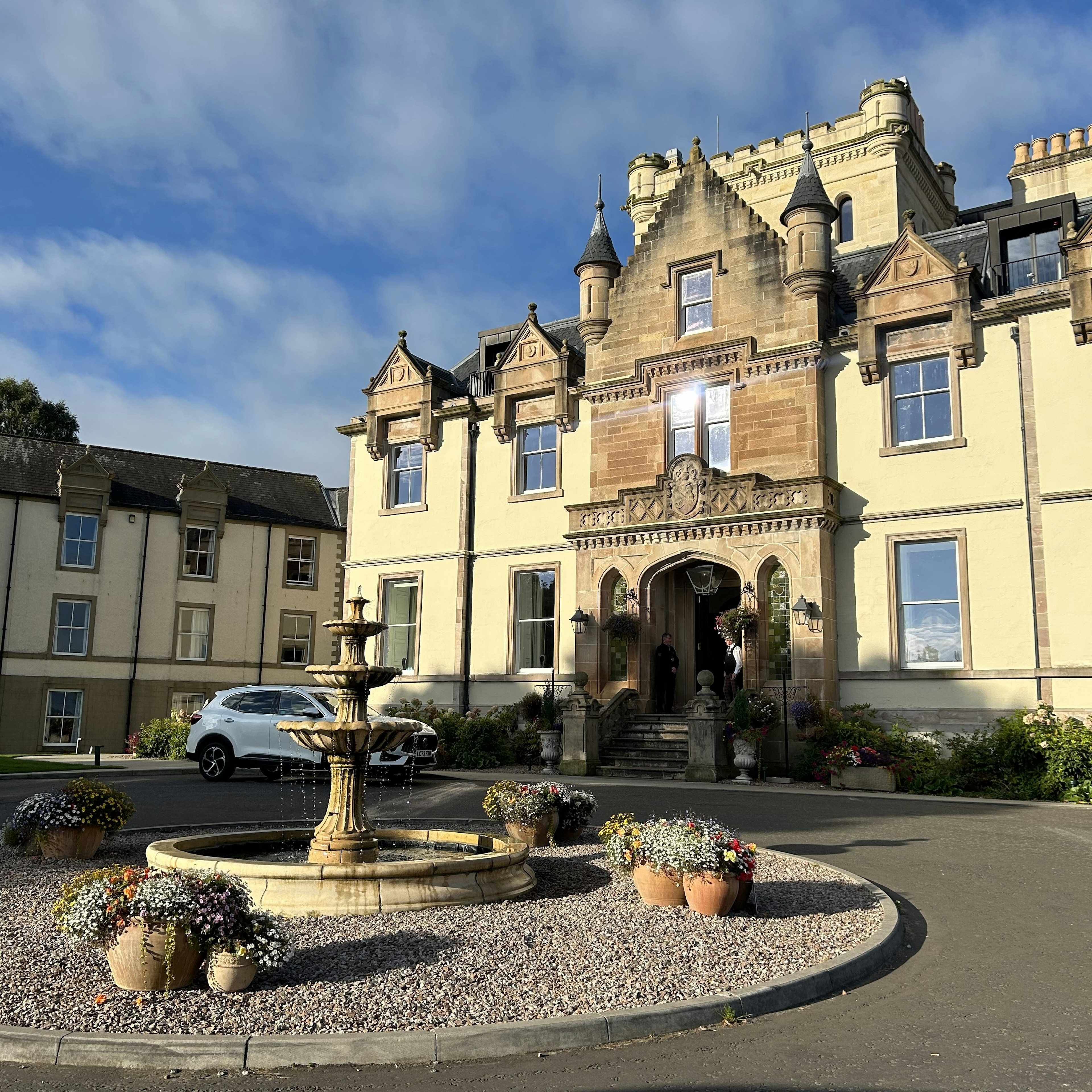 A driveway curves around a fountain in front of a hotel in a historic building.