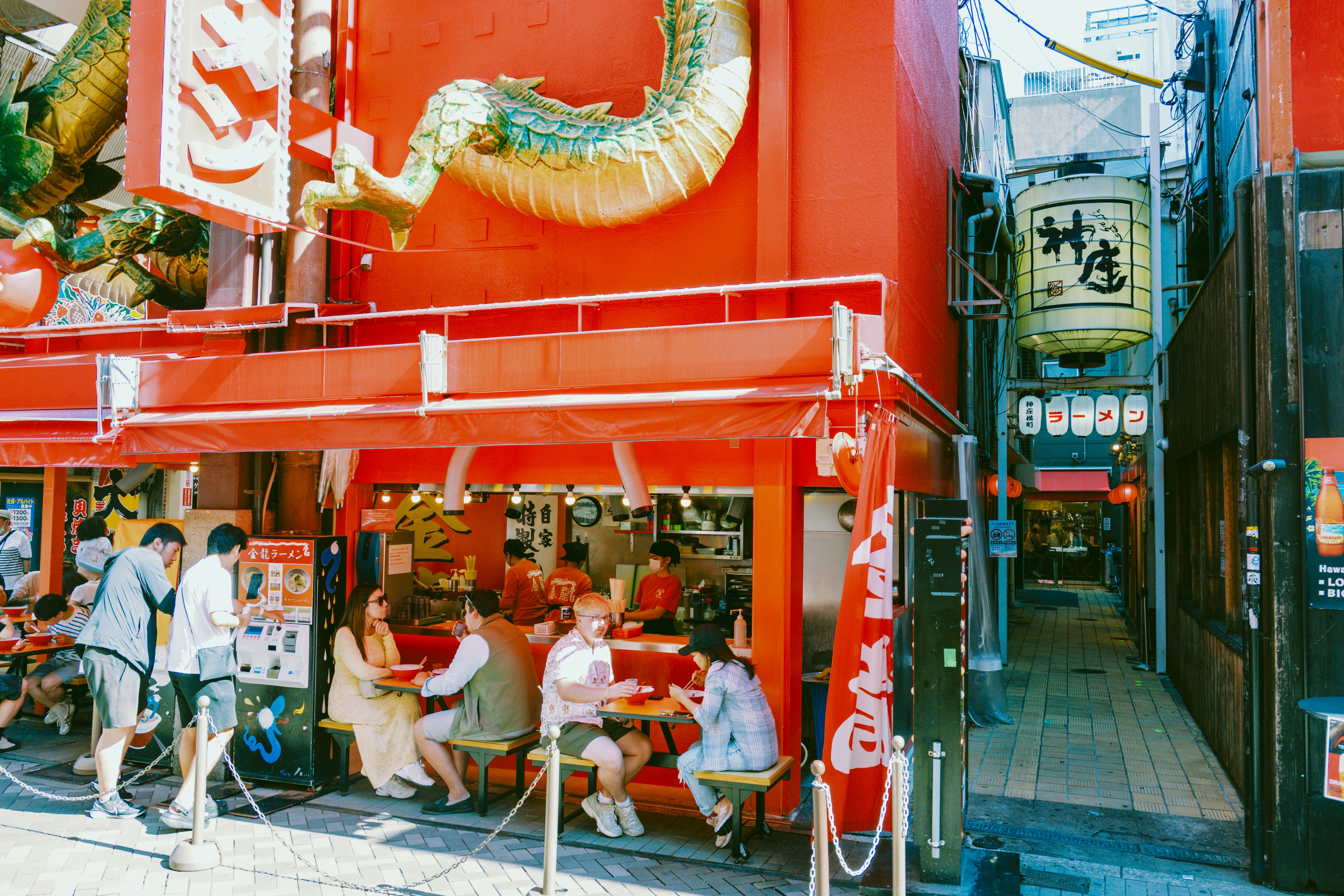 People eat at two streetside tables outside a red restaurant.