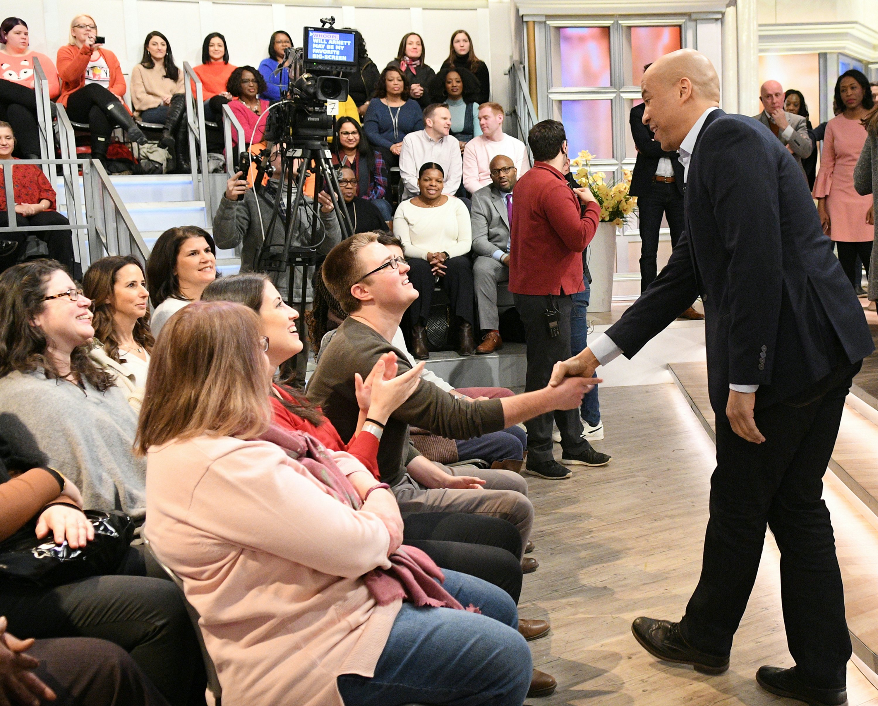 US Senator Corey Booker shakes the hand of an audience member in a television studio.