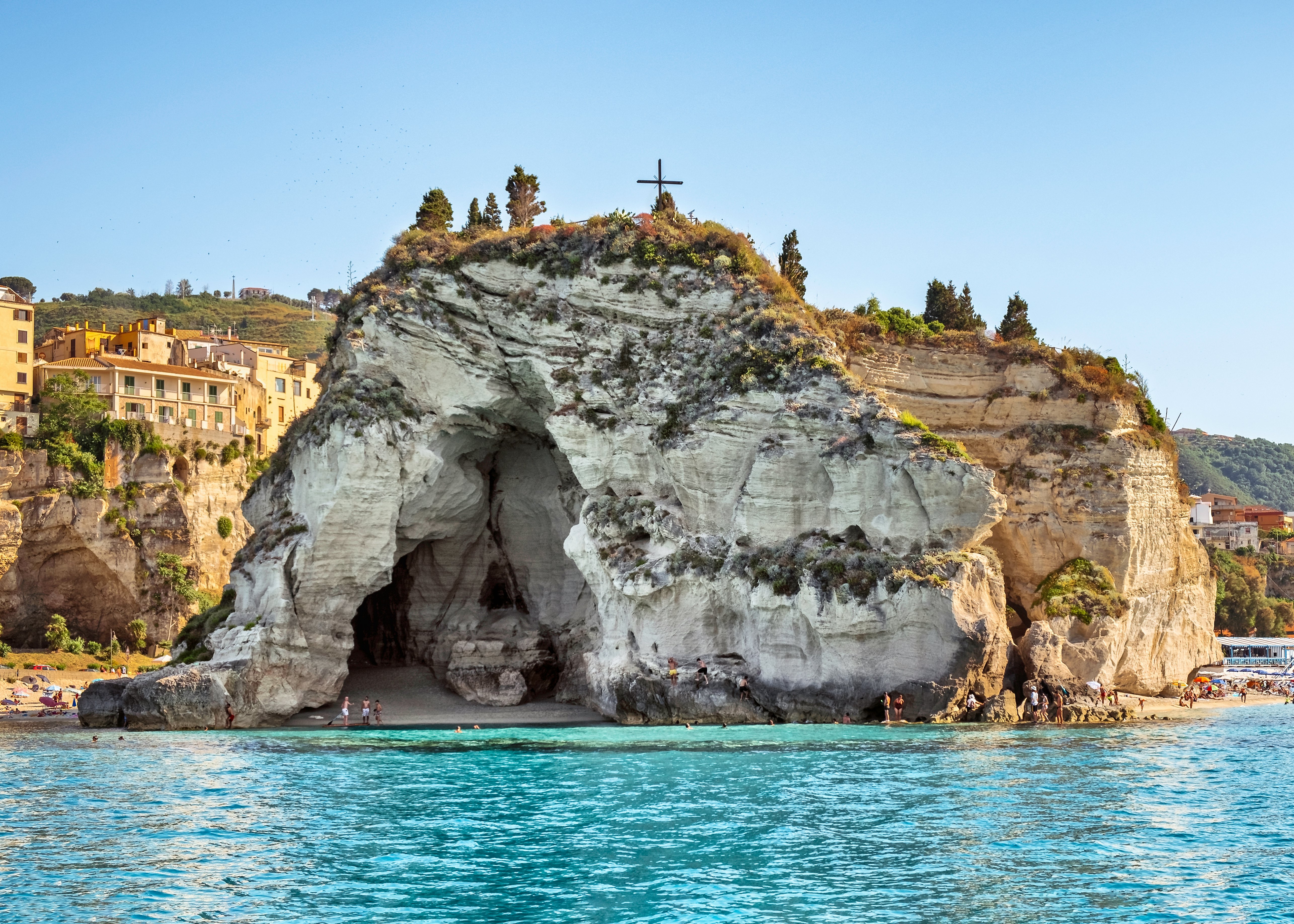 A cave within a cliff with people heading towards the sandy beach.
