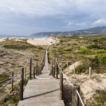 GettyImages-1484891918.jpg
Empty, wooden boardwalk on a beach Praia do Guincho in Sintra. View of grass and sand with hills and Atlantic Ocean in the background
