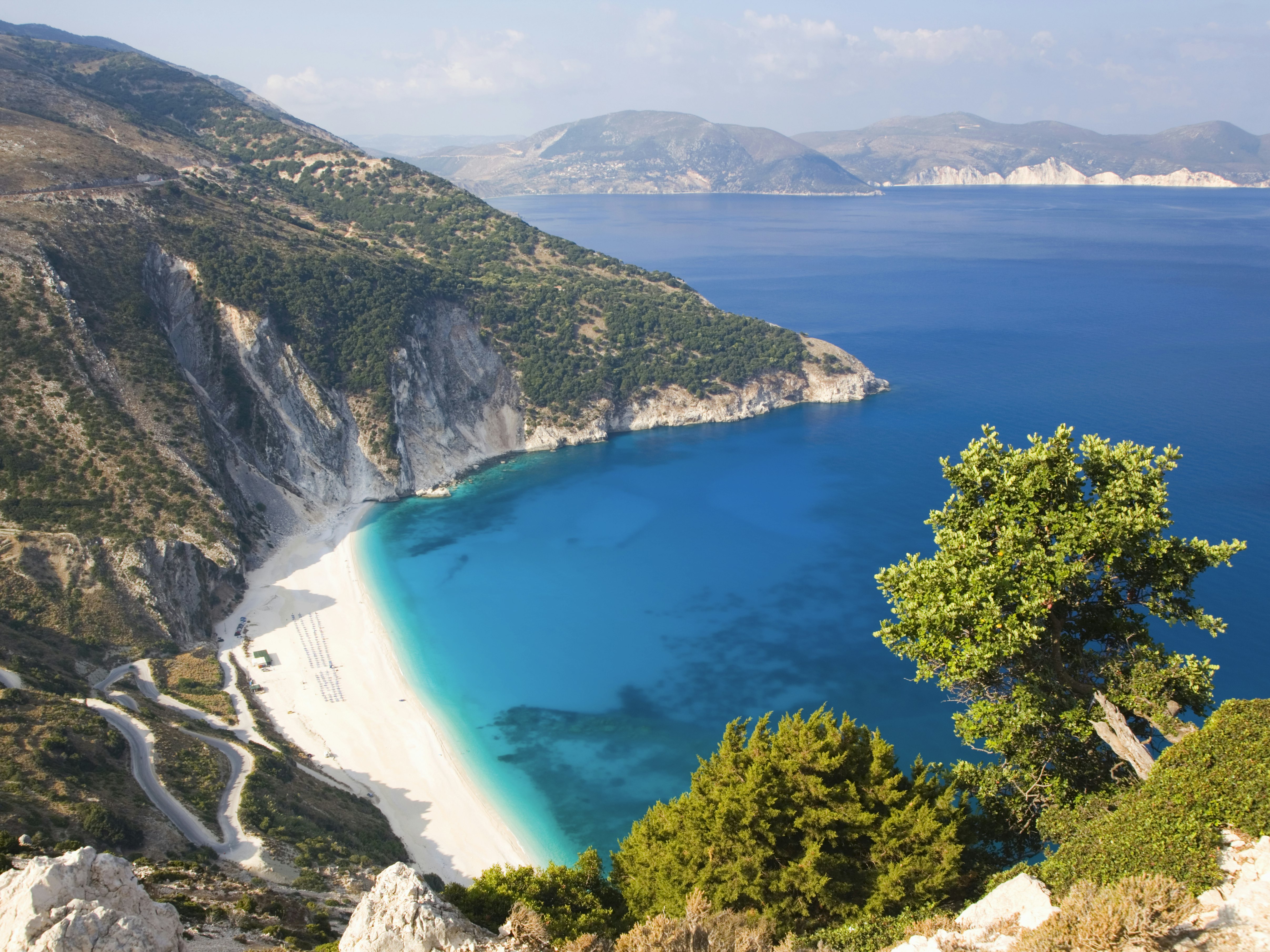A curve of white sand below steep cliffs. The calm turquoise sea laps at the shore.