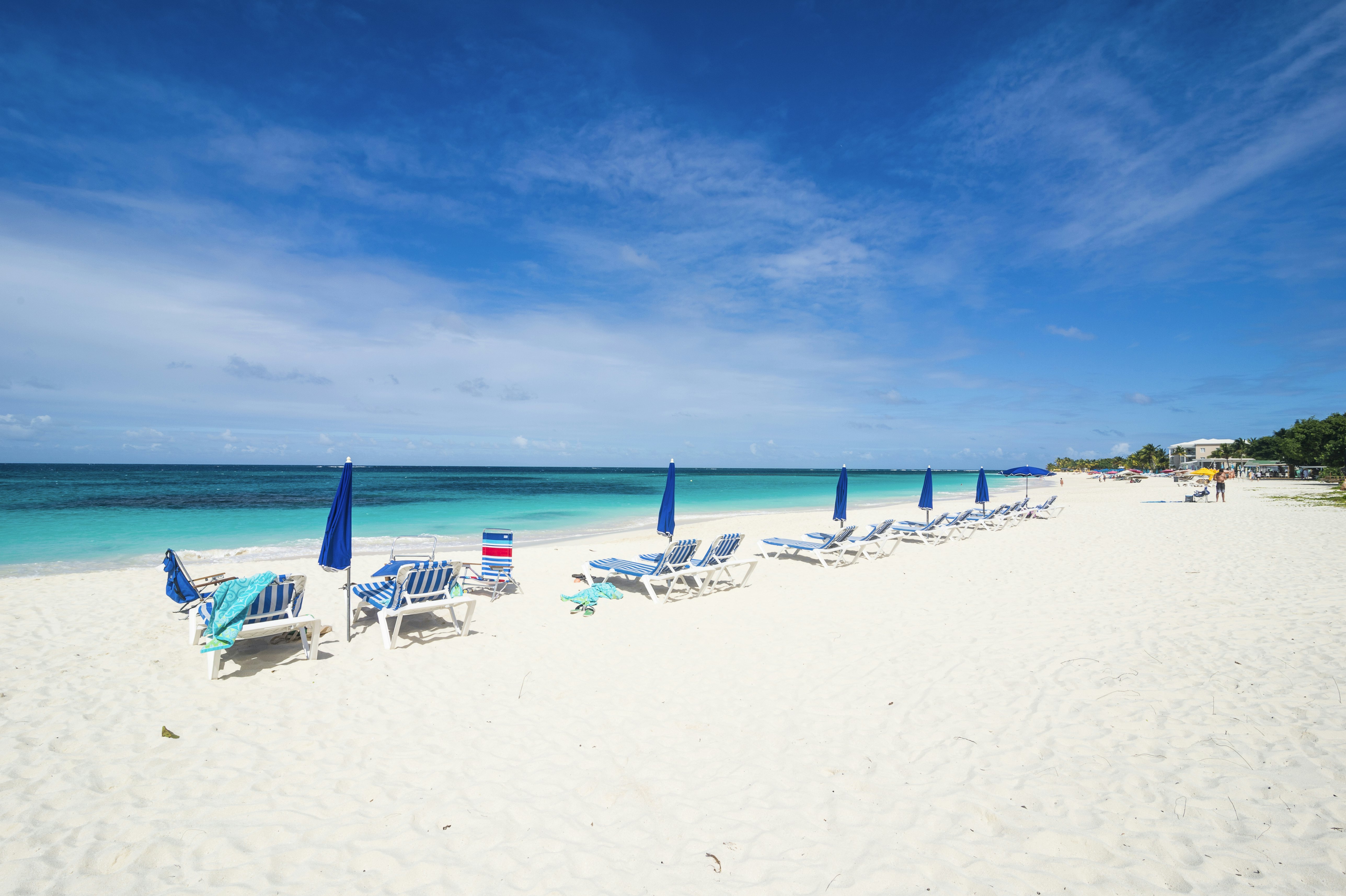 A row of blue and white striped sun loungers with blue sun umbrellas on a white-sand beach.