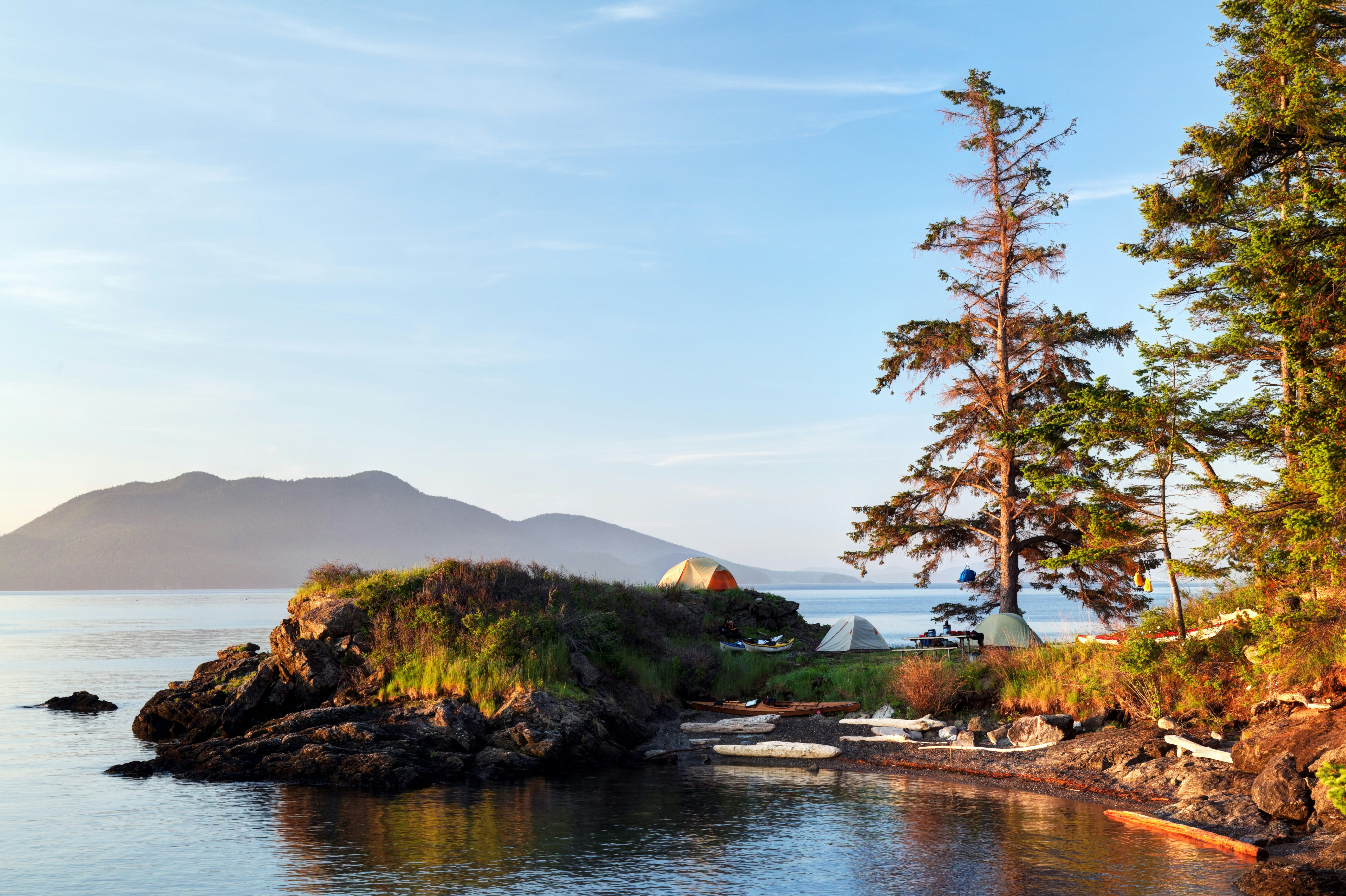 Three tent pitched on a rocky island shoreline at sunrise.