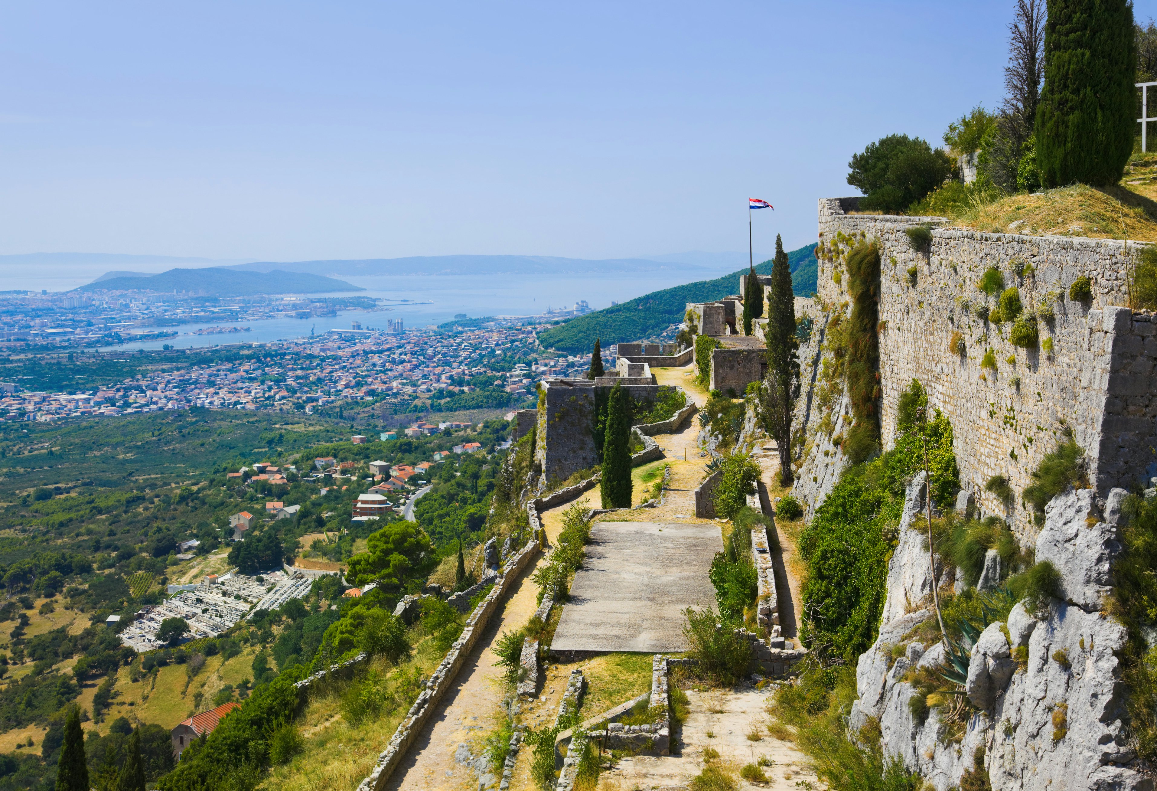 The ruins of a hilltop fortress with views down to a coastal town and distant islands.