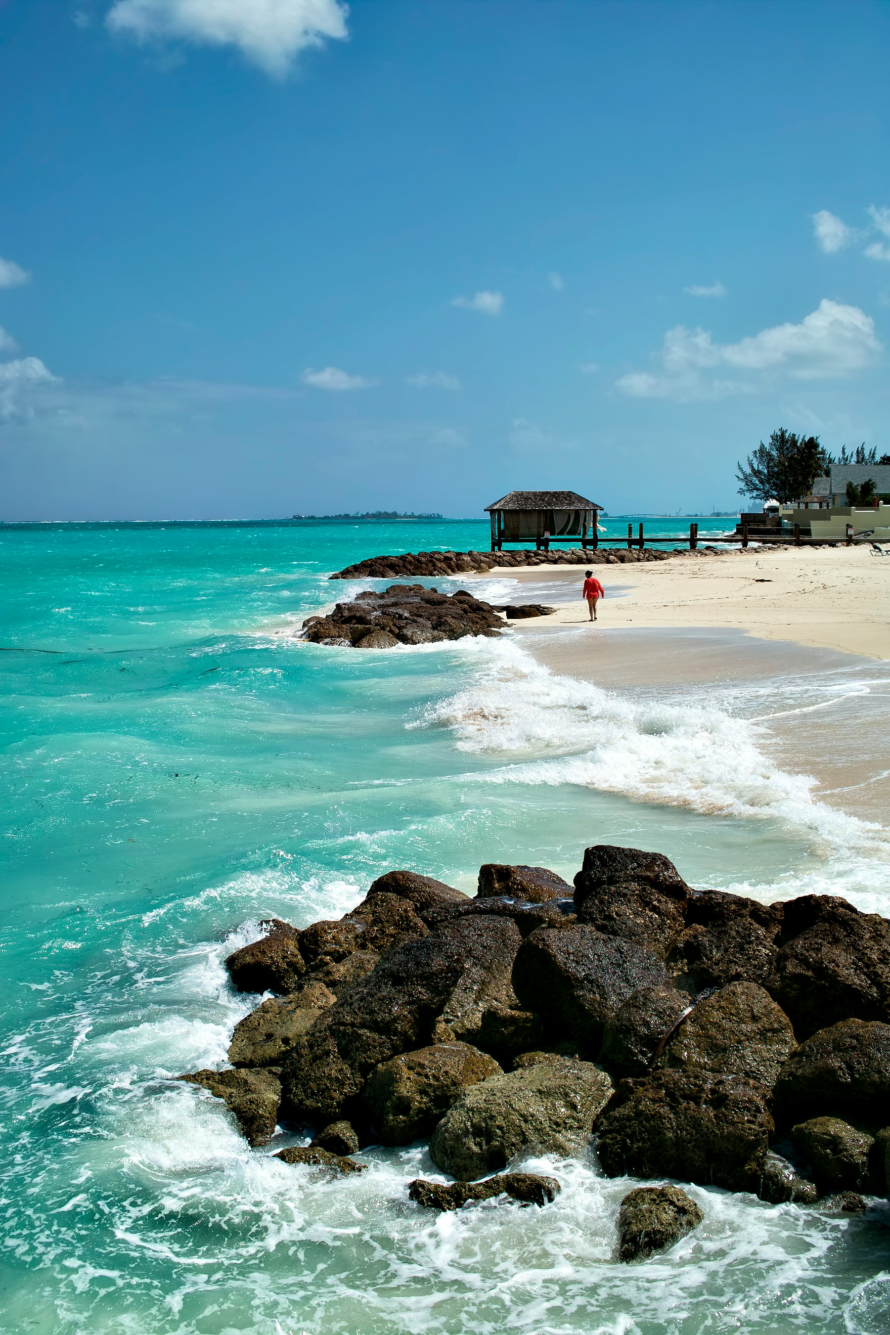 Someone walks toward a thatched hut on the beach in Nassau, Bahamas.