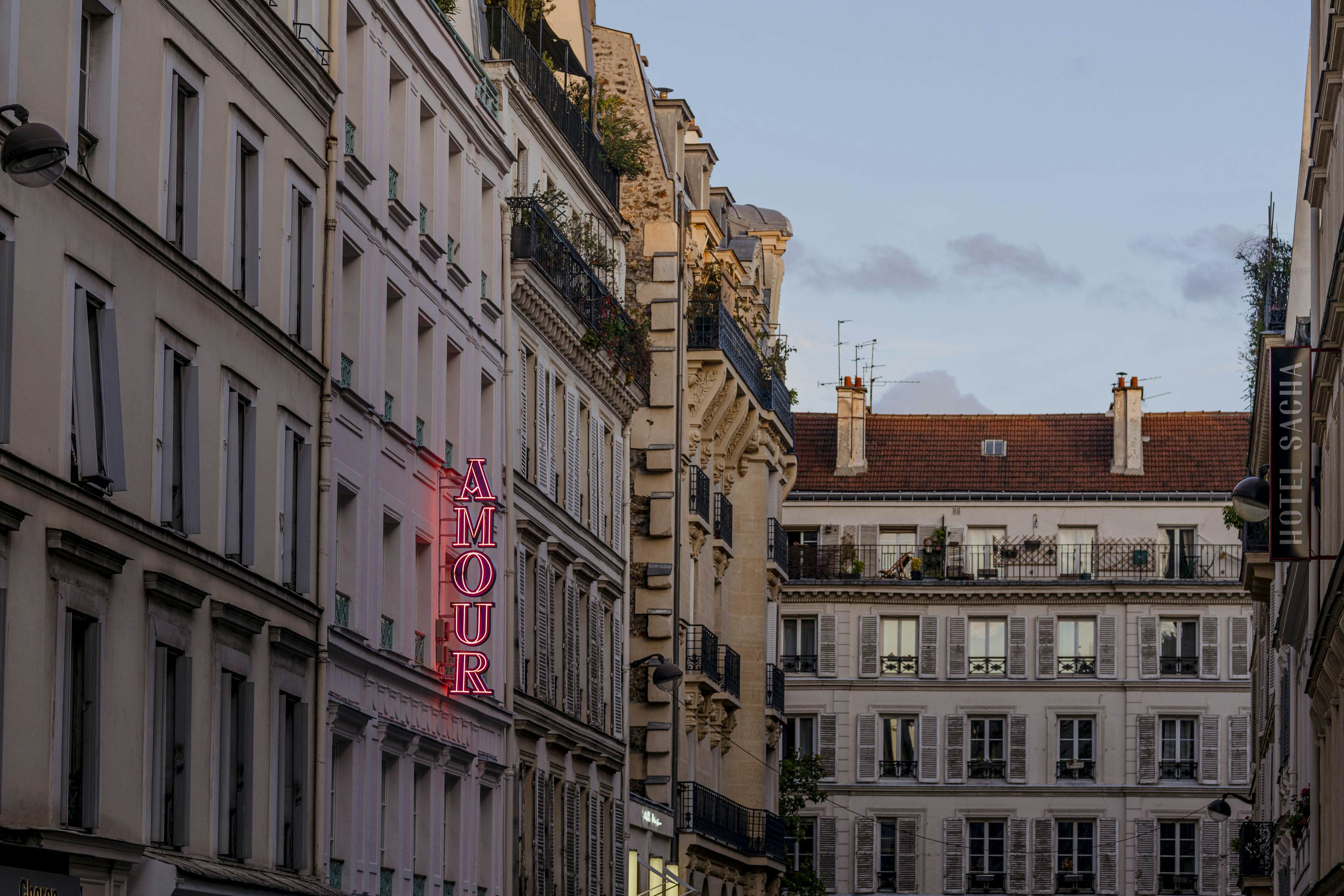 A vertical pink neon sign on a building reads "Amour."