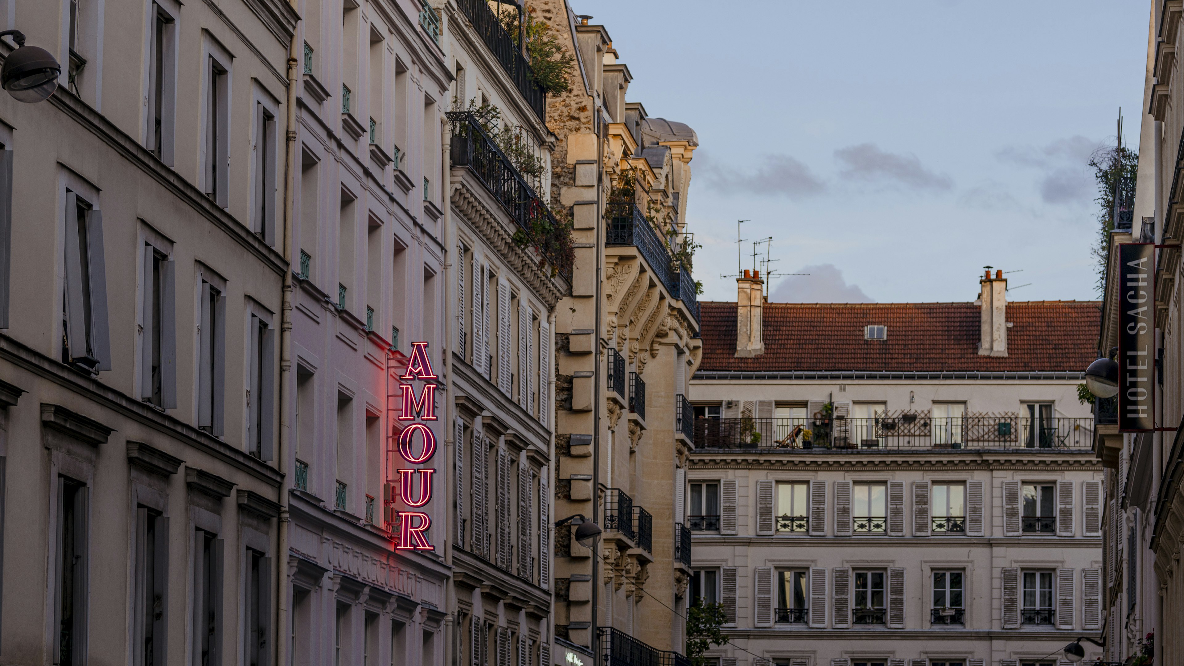 A vertical pink neon sign on a building reads "Amour."