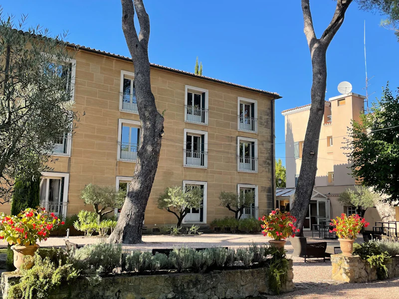 A tan stone building with trees and plants in front of it.