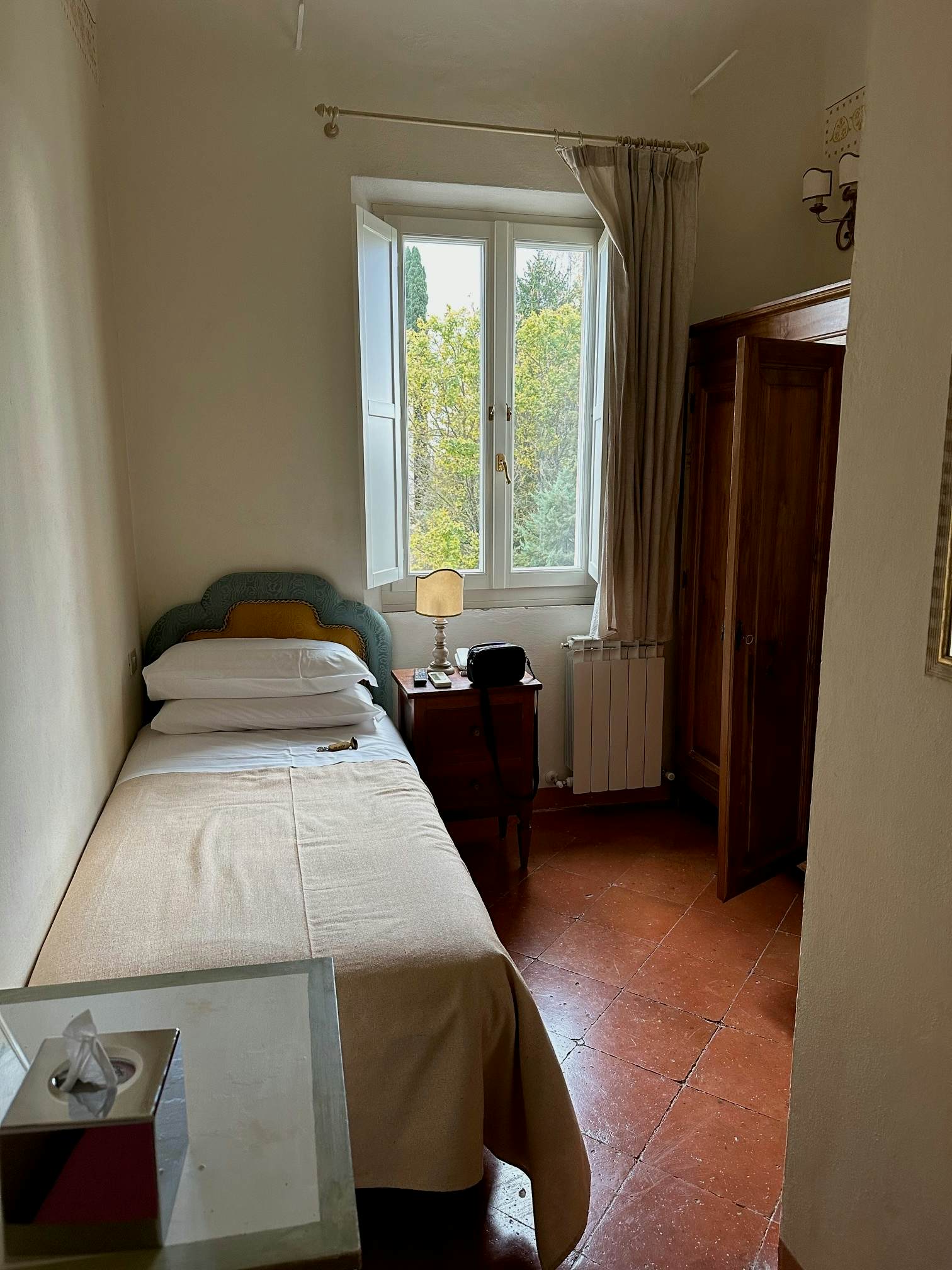 A single bed in a simple narrow room with a window.