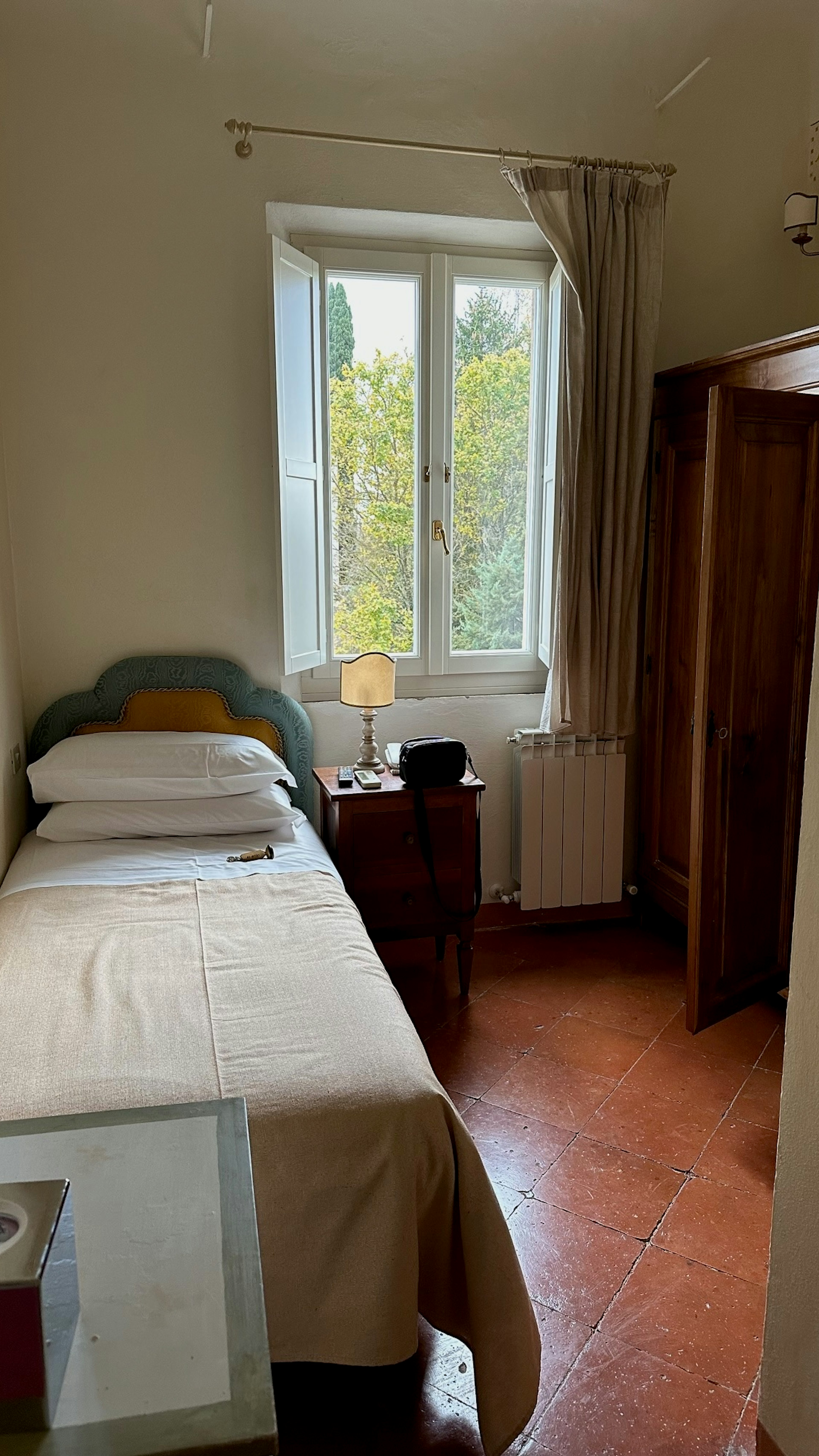A single bed in a simple narrow room with a window.