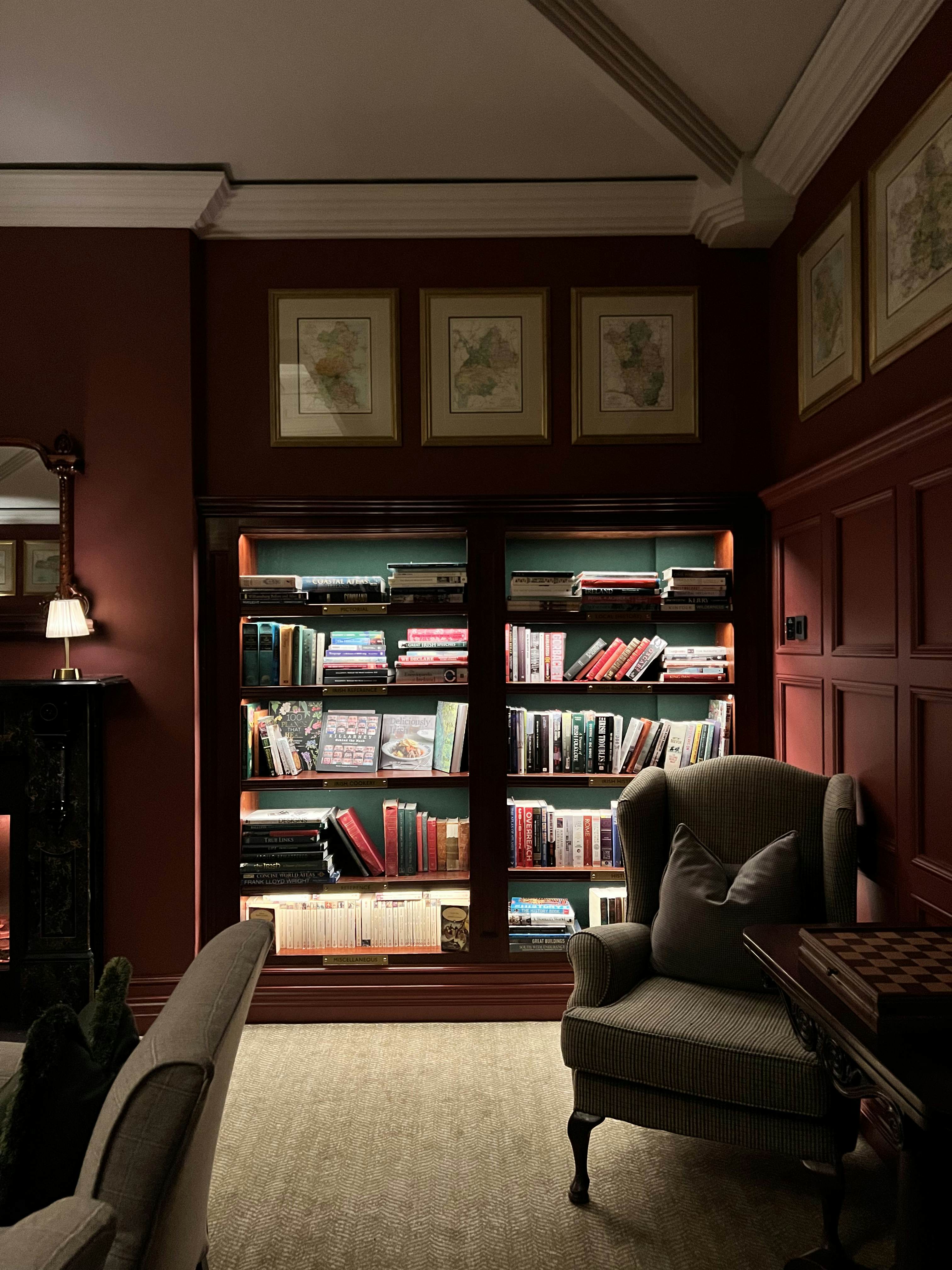 An armchair in front of a bookcase with interior lights on the shelves.