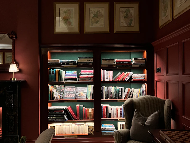 An armchair in front of a bookcase with interior lights on the shelves.