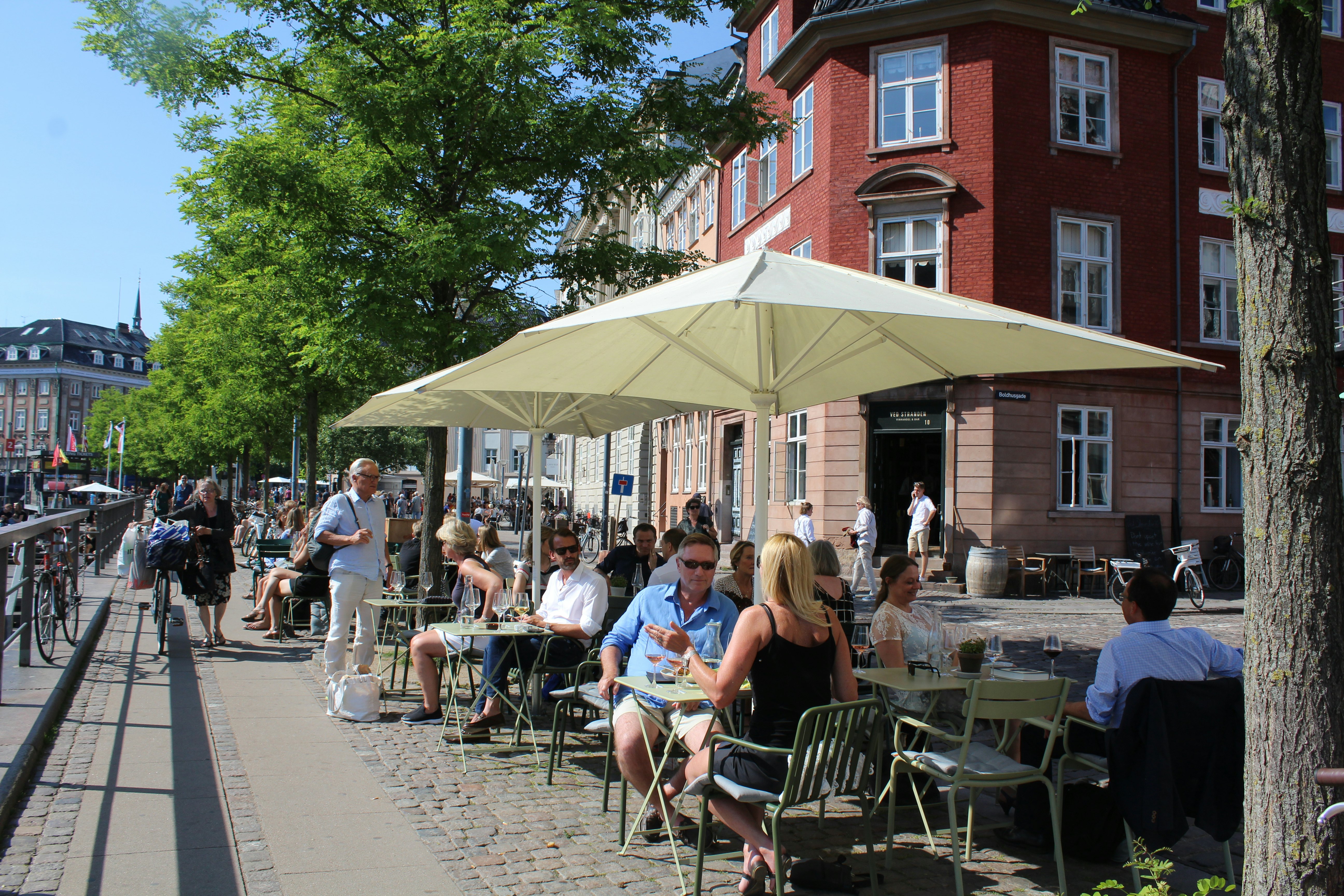 People sit in the sun at an outdoor cafe with umbrellas.