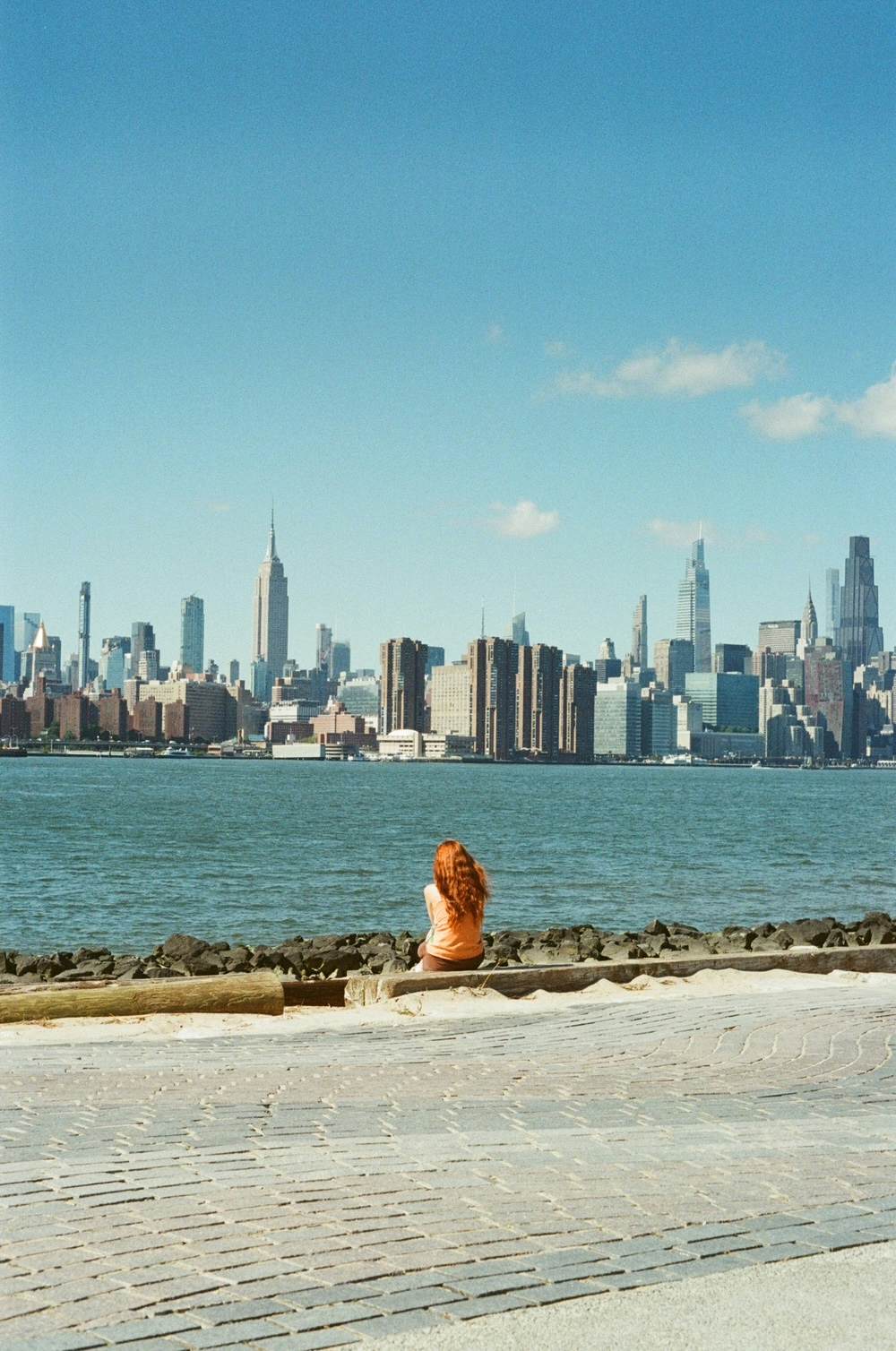 A person with red hair looks out over a river at a city skyline