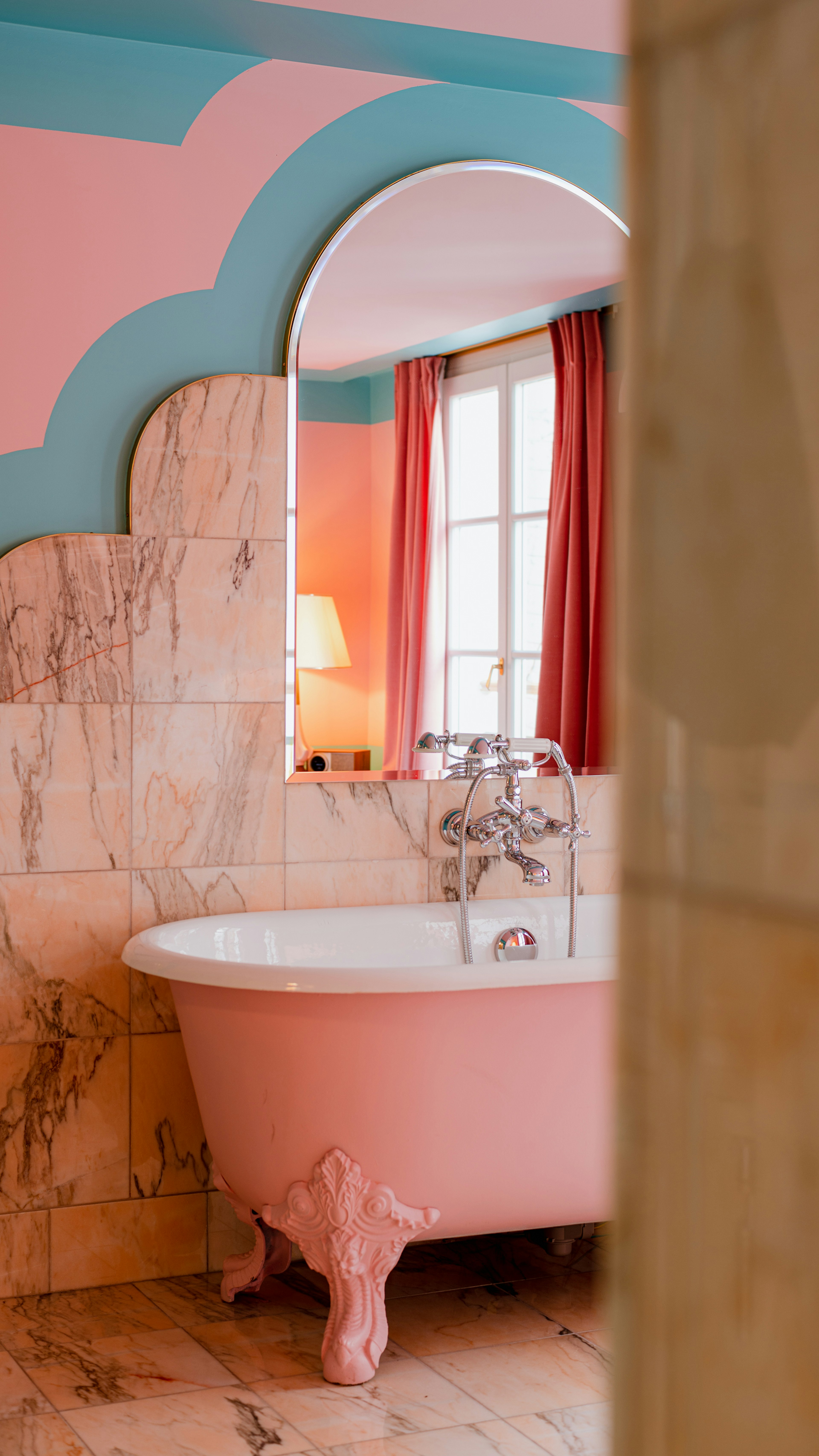 A pink claw-foot tub in a room with veined marble walls.