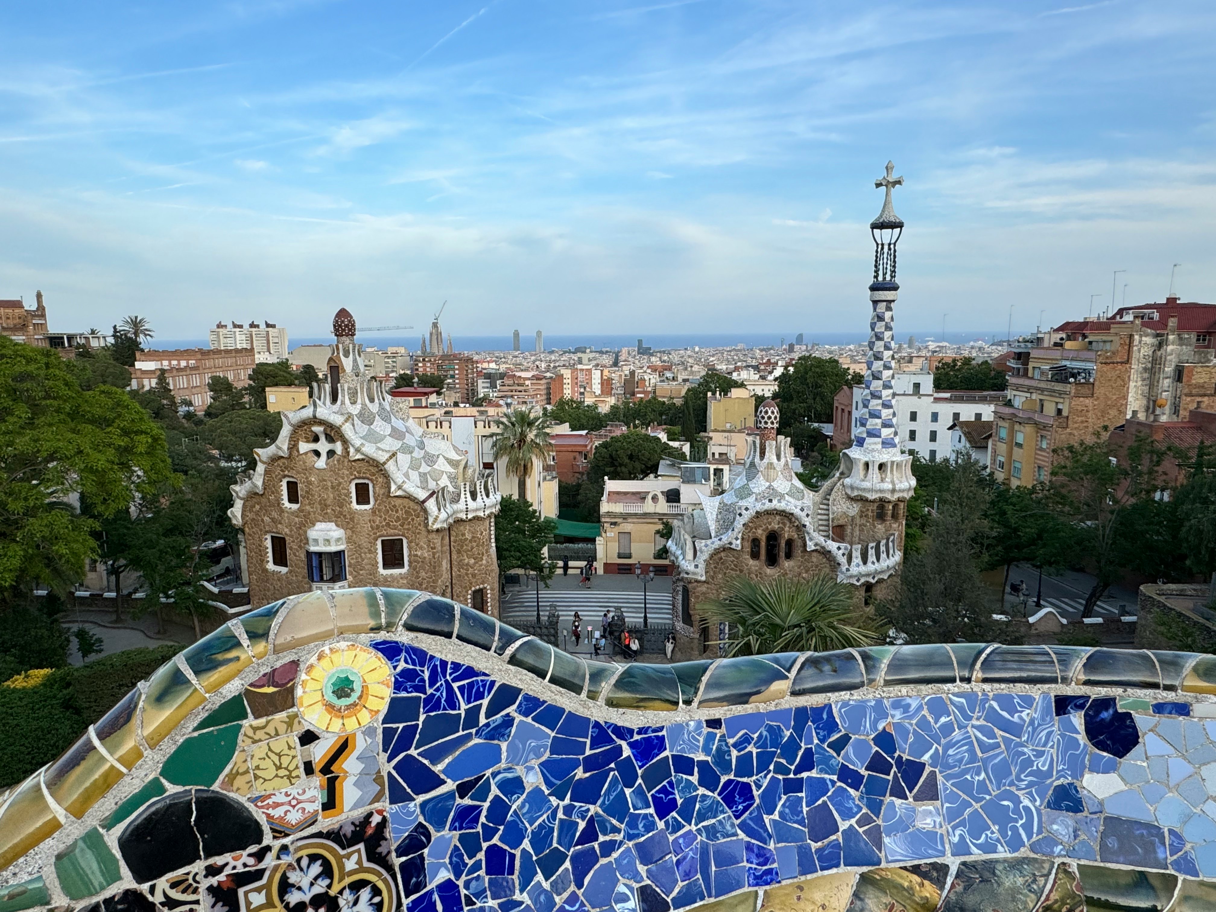 A colorful mosaic bench in the foreground gives way to a city landscape; the sea is on the horizon.