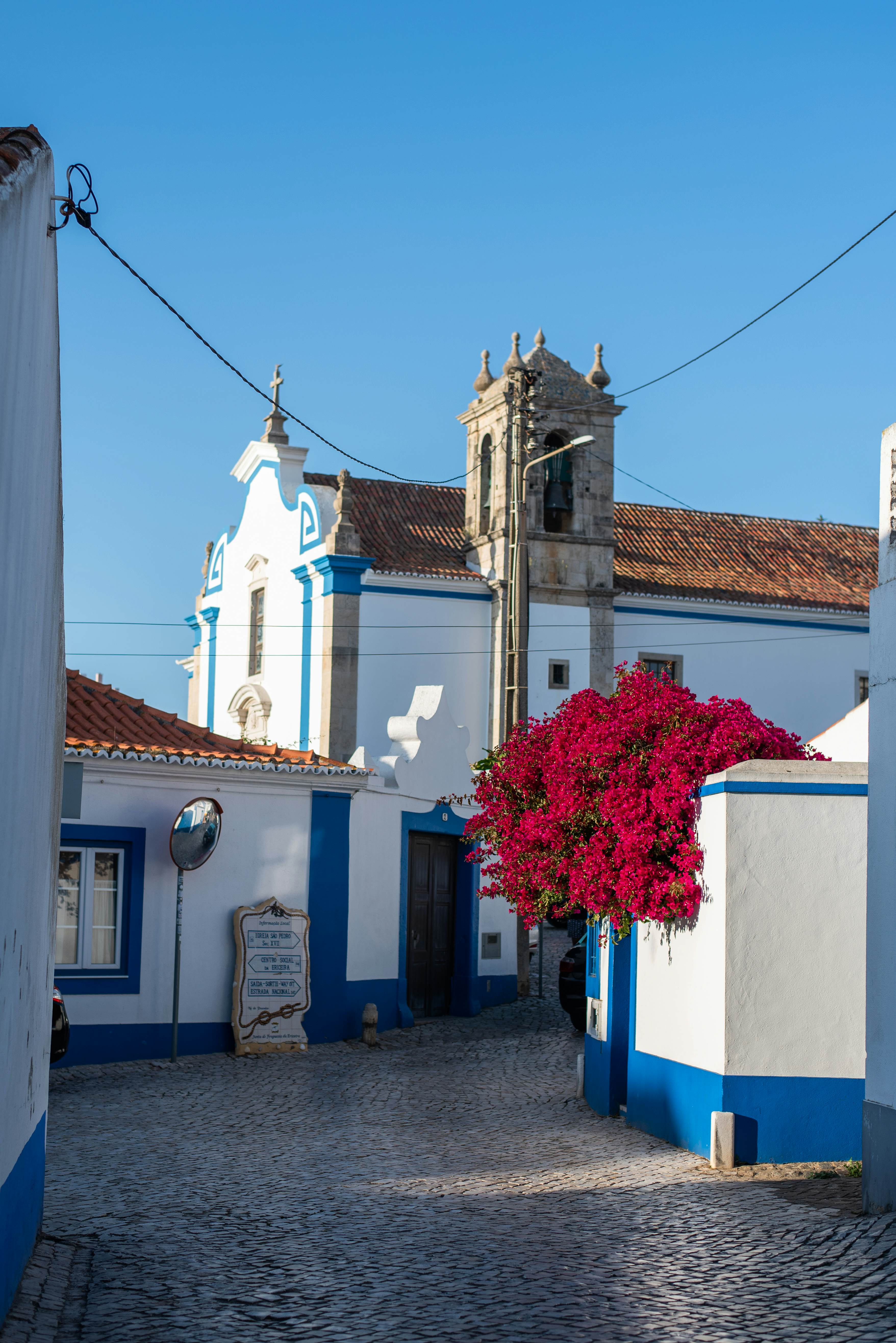 A cobbled street through a small village where whitewashed buildings are trimmed with blue paint.