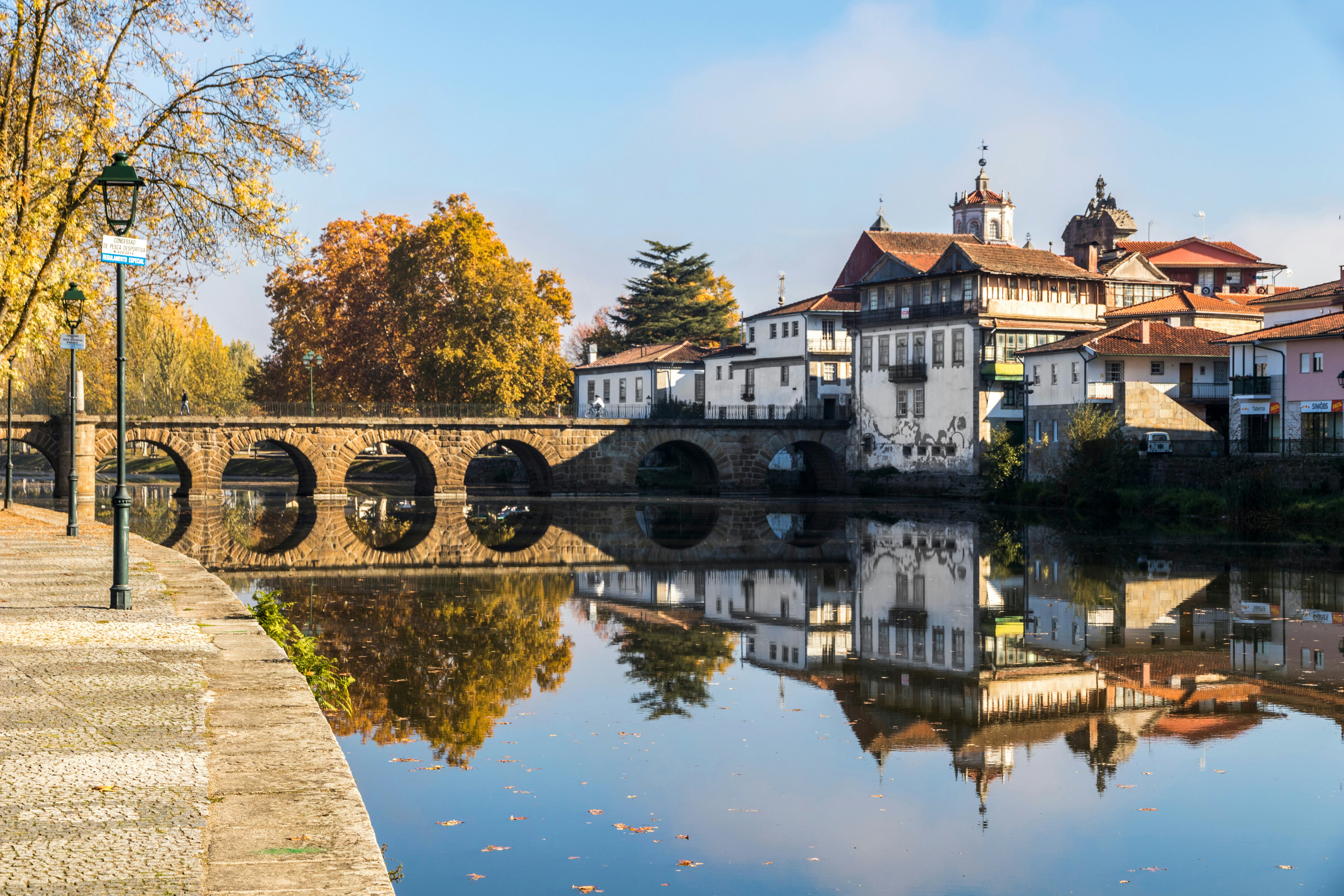 A stone bridge reflected in a calm river through a small town.