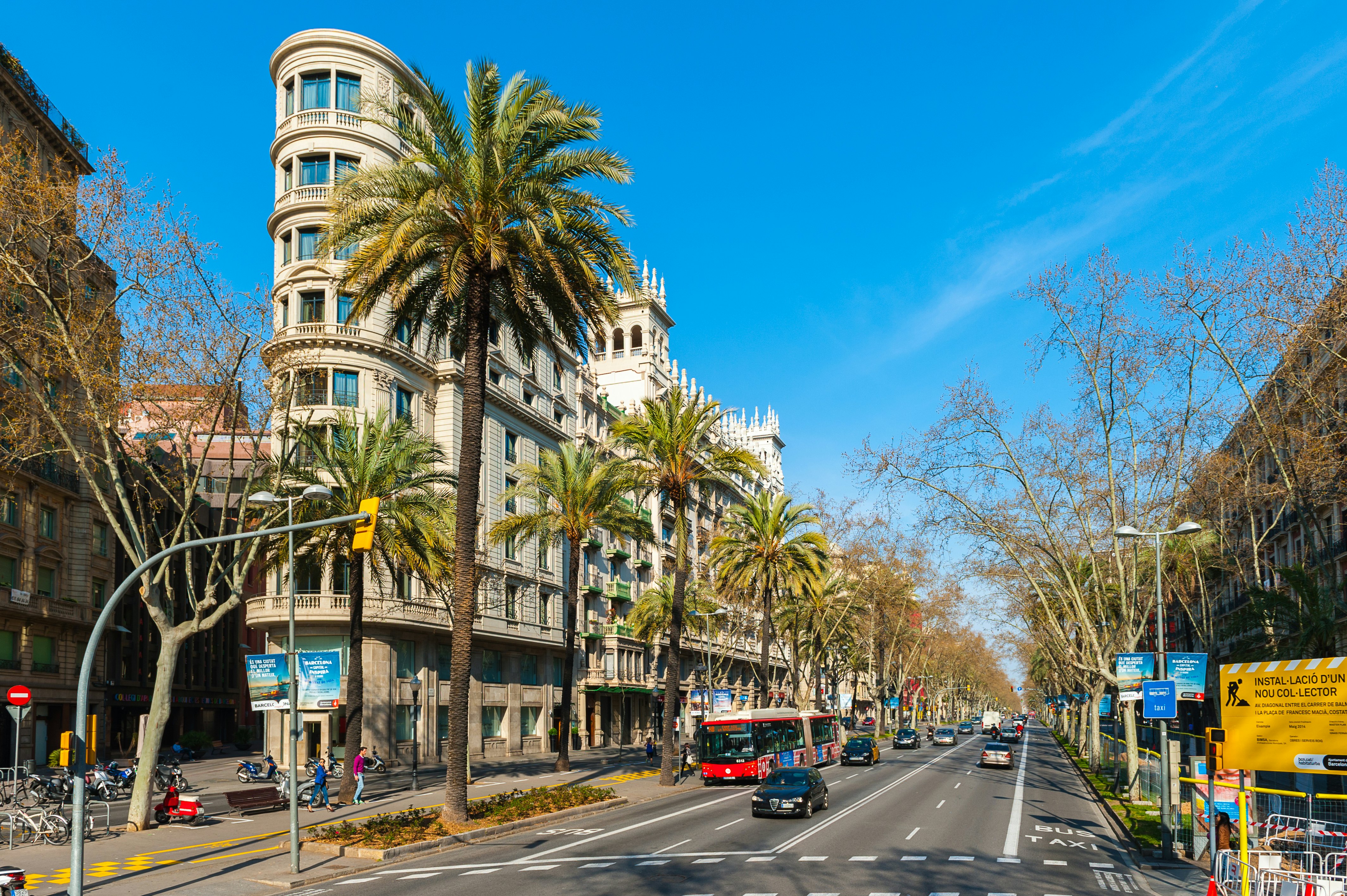Buses and cars pass along Passeig de Gràcia in Barcelona, Spain, with palms and striking buildings overhead.