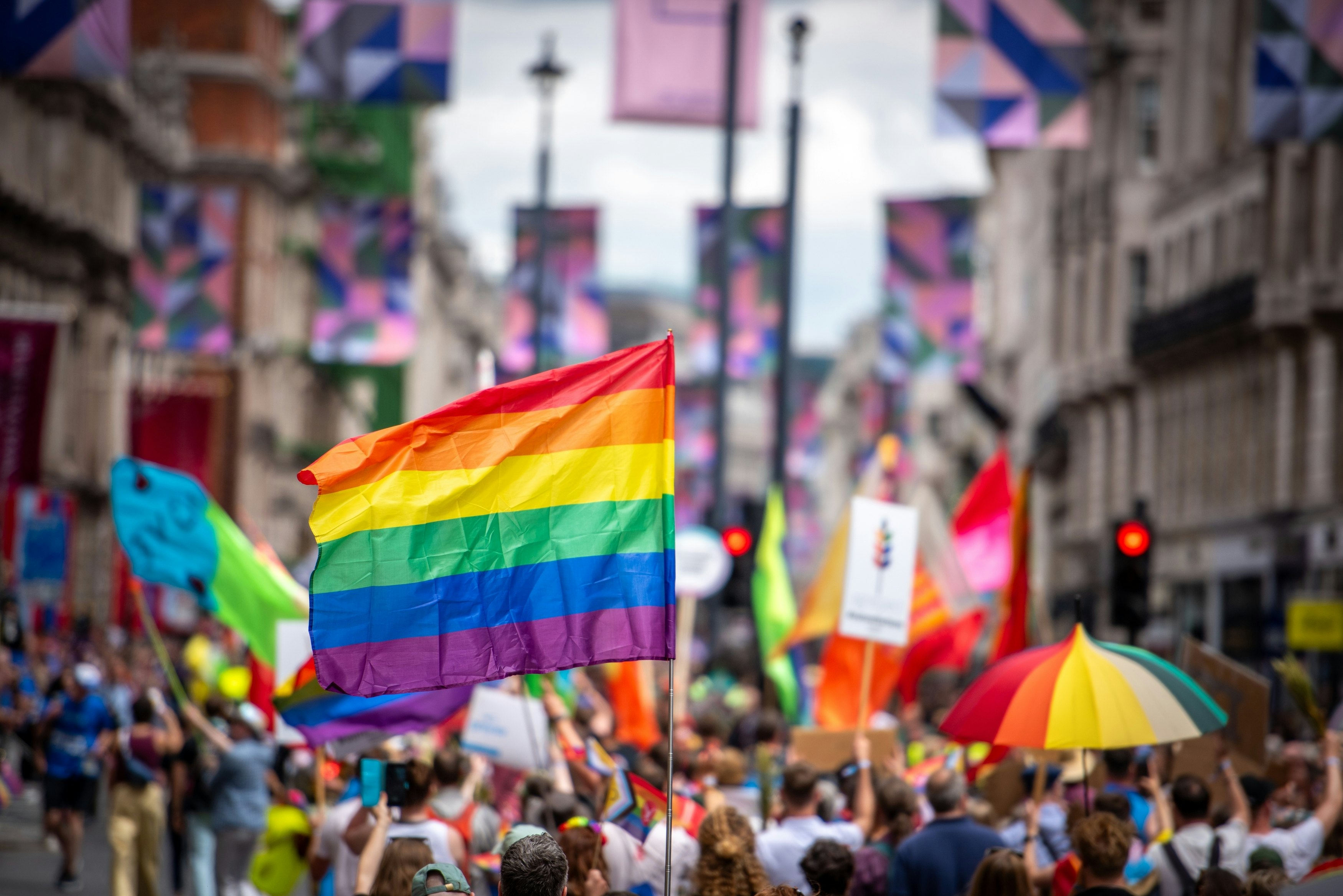 Crowds of people walk down a street together waving rainbow flags.