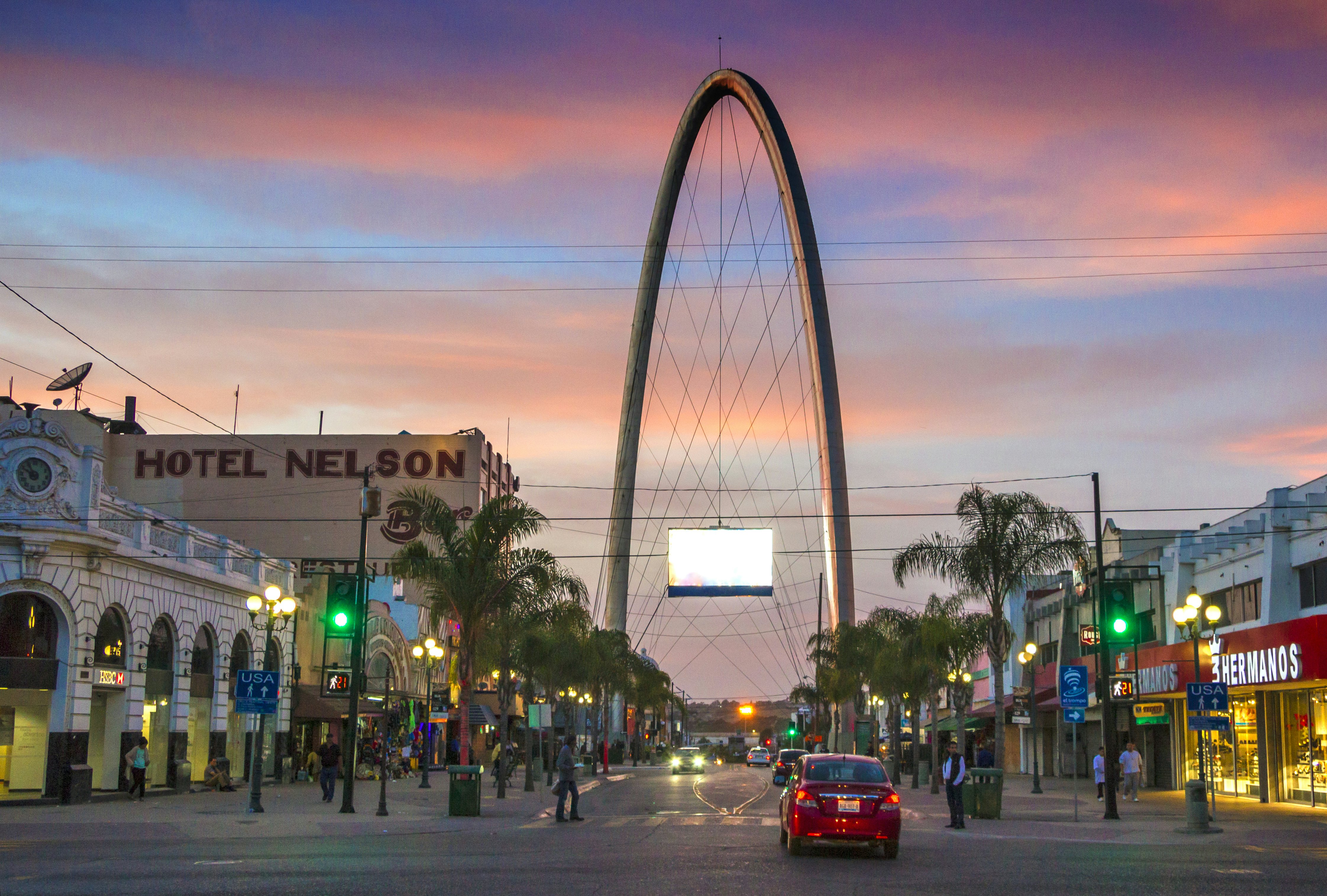 A tall arch is seen at the end of a wide city street at dusk.