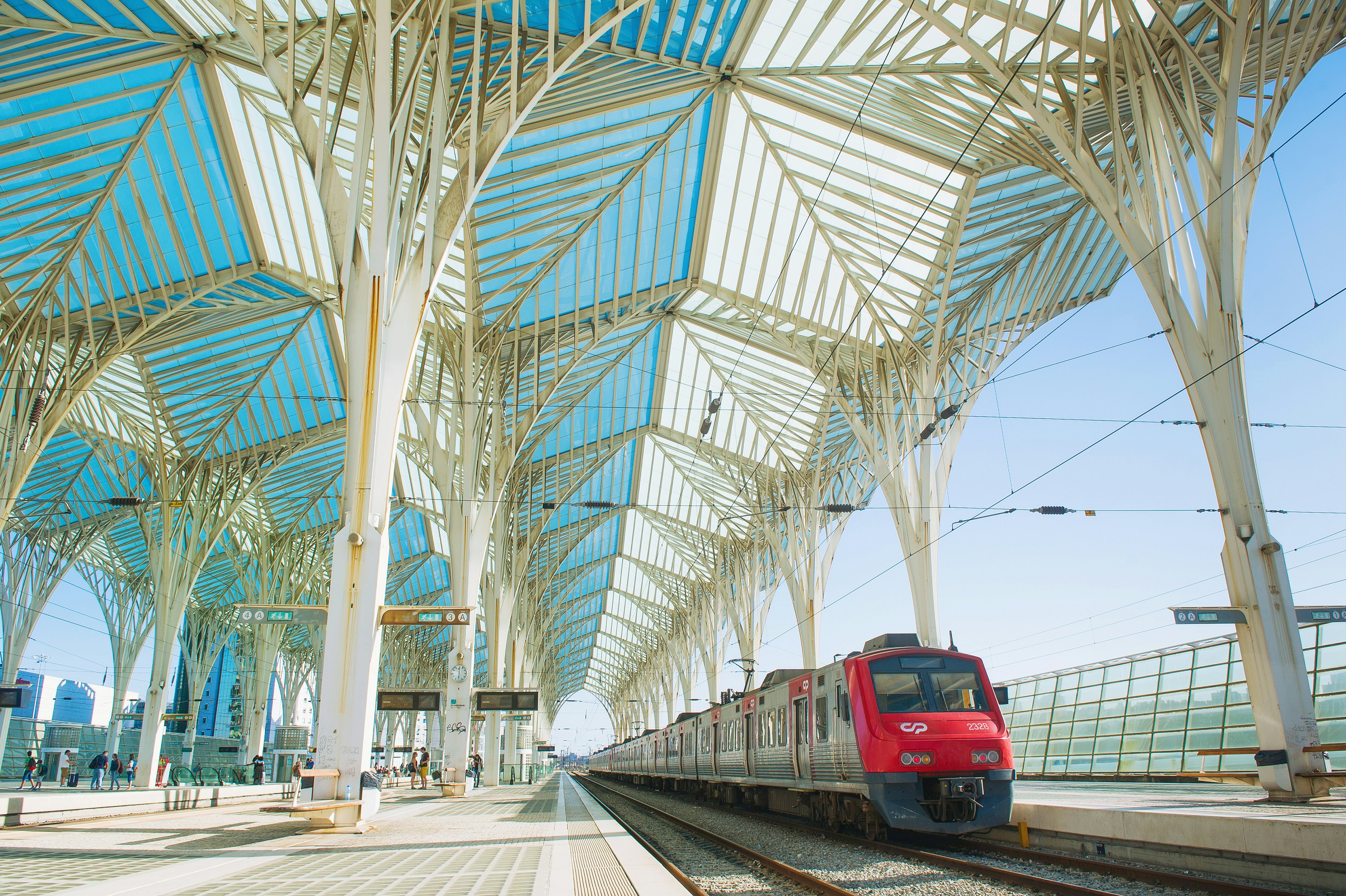A railway platform with metal and glass lattice covering it. A red and silver train is stopped at the platform.