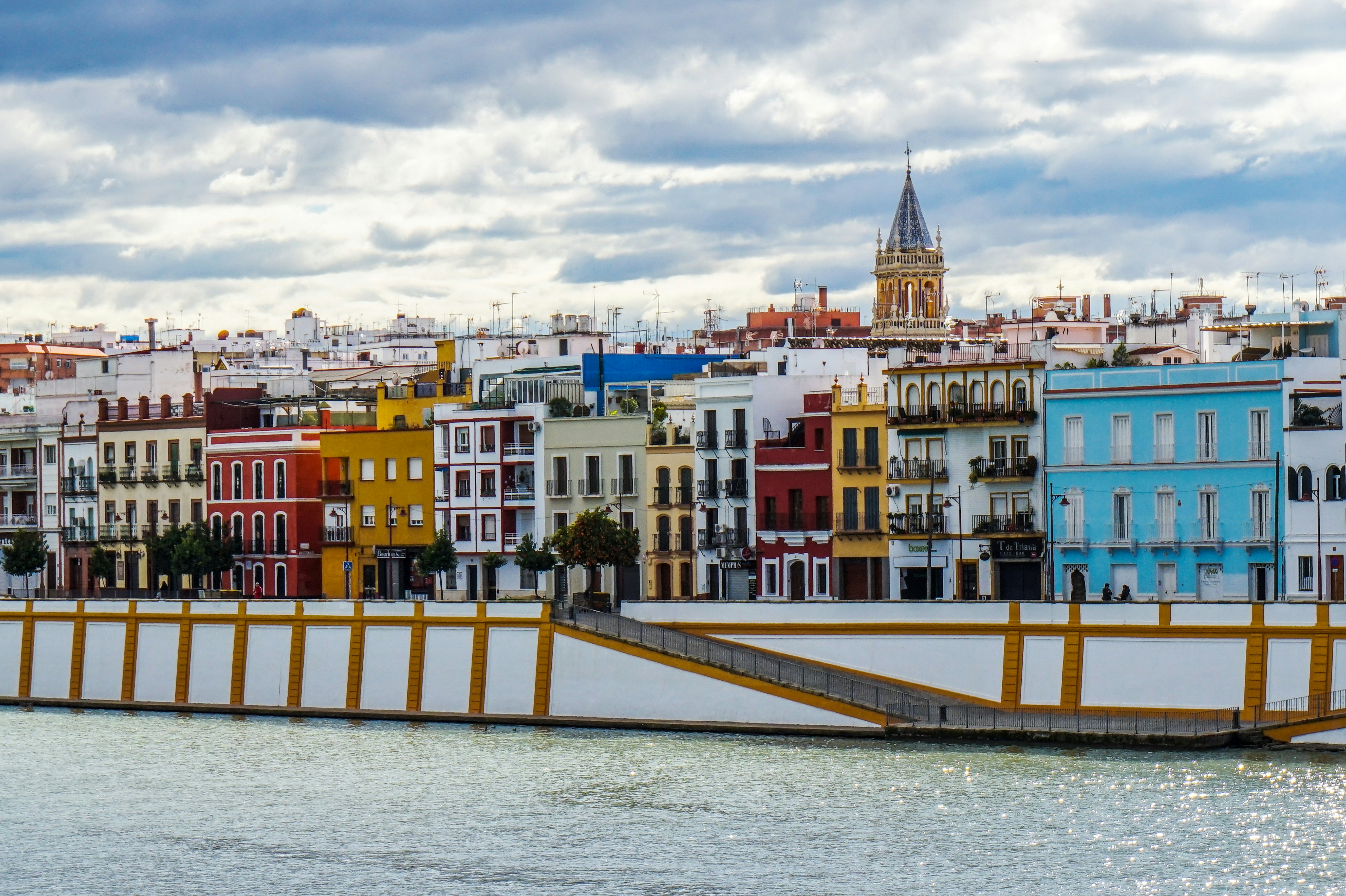 Colorful buildings sit along a street along a riverfront in a city.