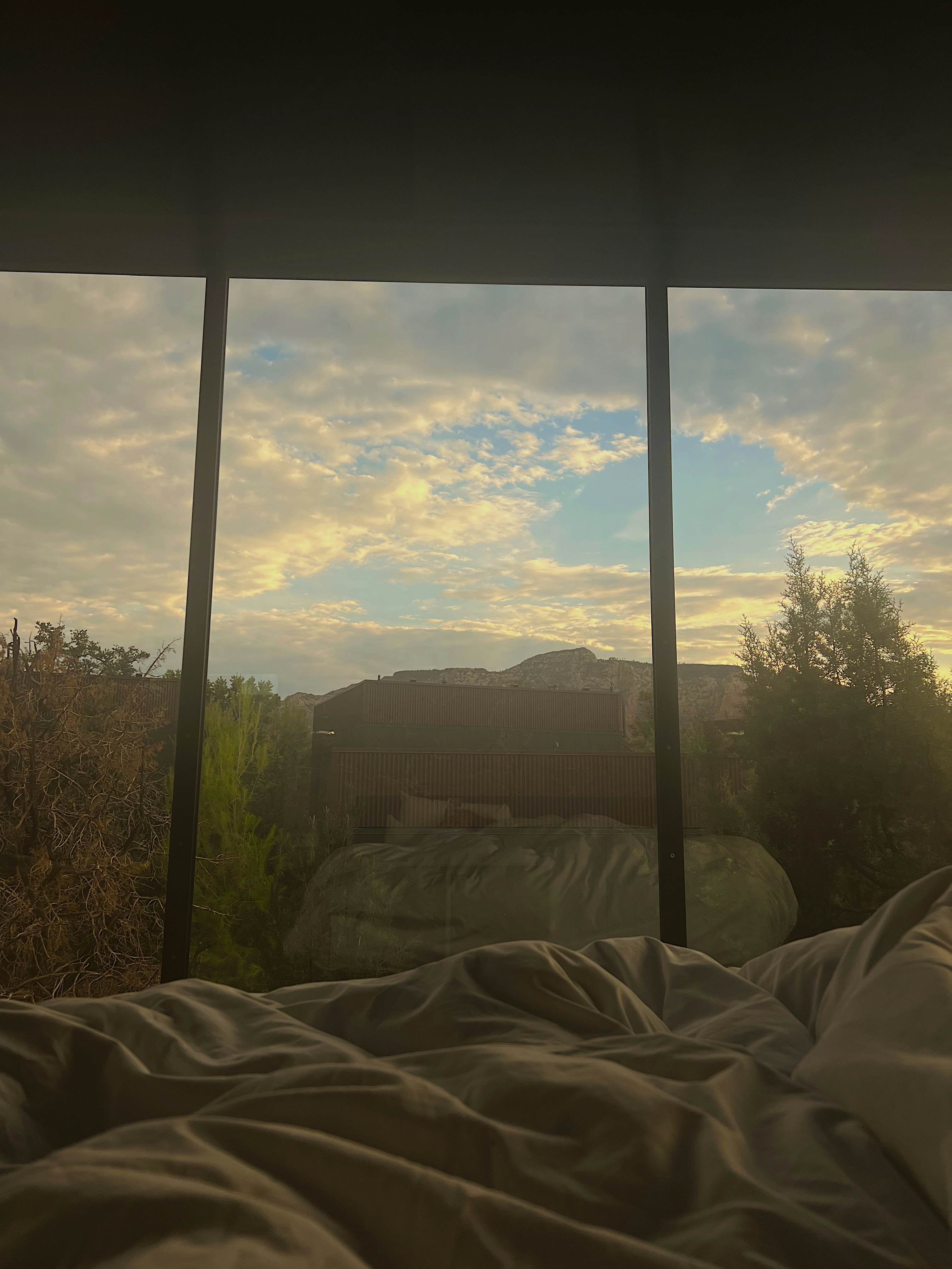 Silhouettes of rock formations in morning light through a window from a hotel bed.