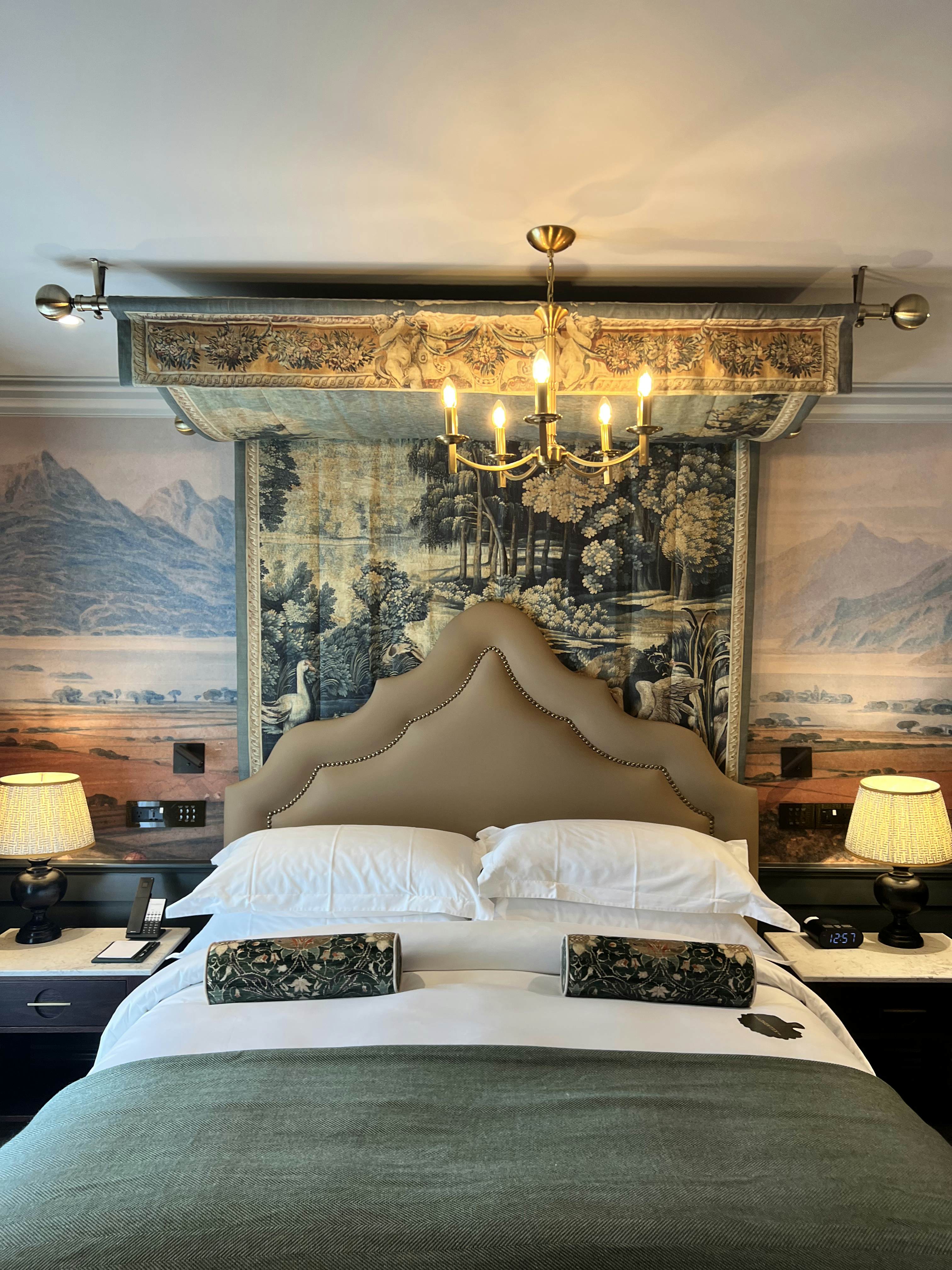 A bed with a white covering and round patterned pillows; the triangular headboard is beige, and the wall behind it has layered pieces of artwork.