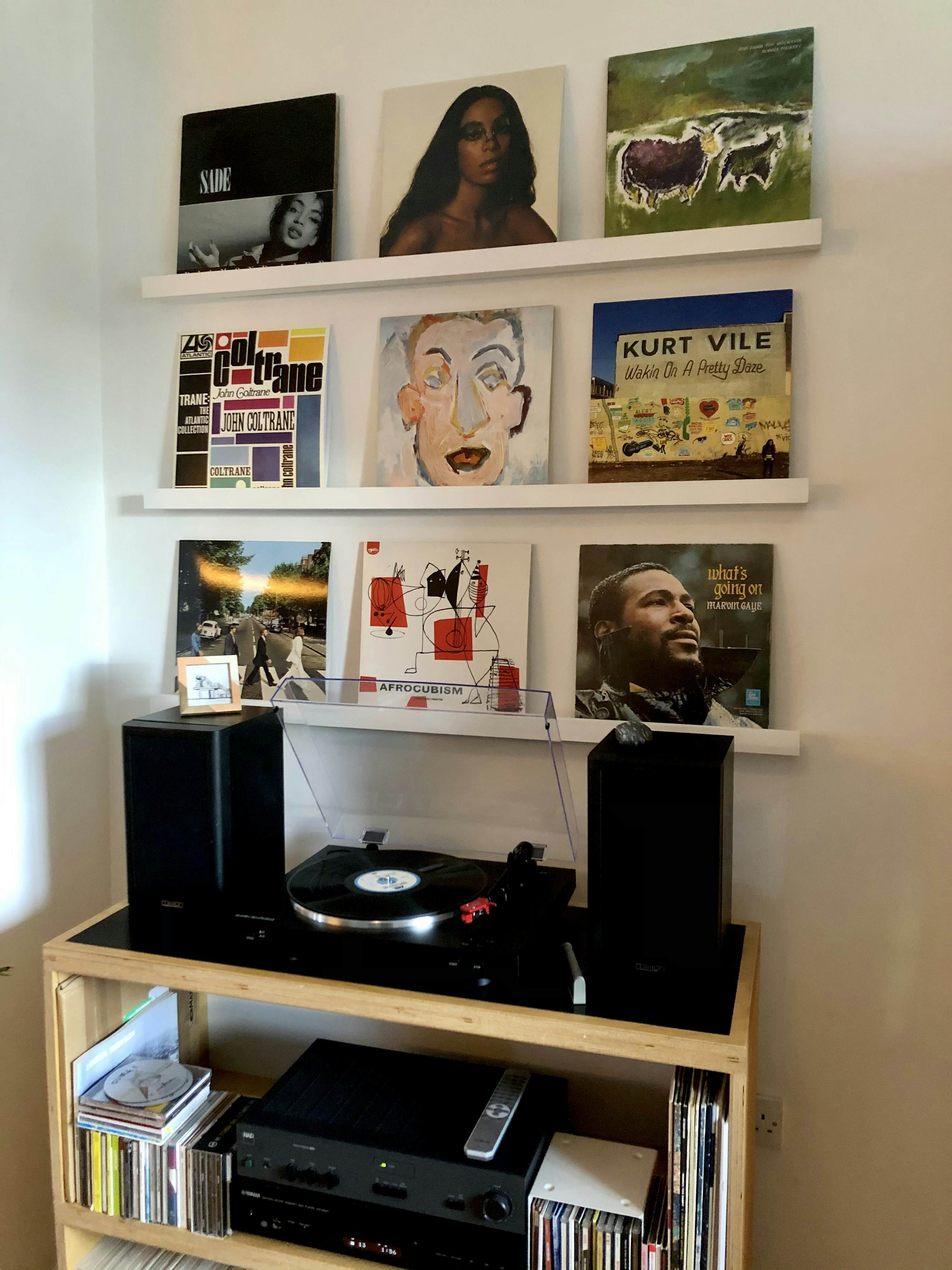 A record player and speakers are on a shelf; six albums are displayed on two shelves above.