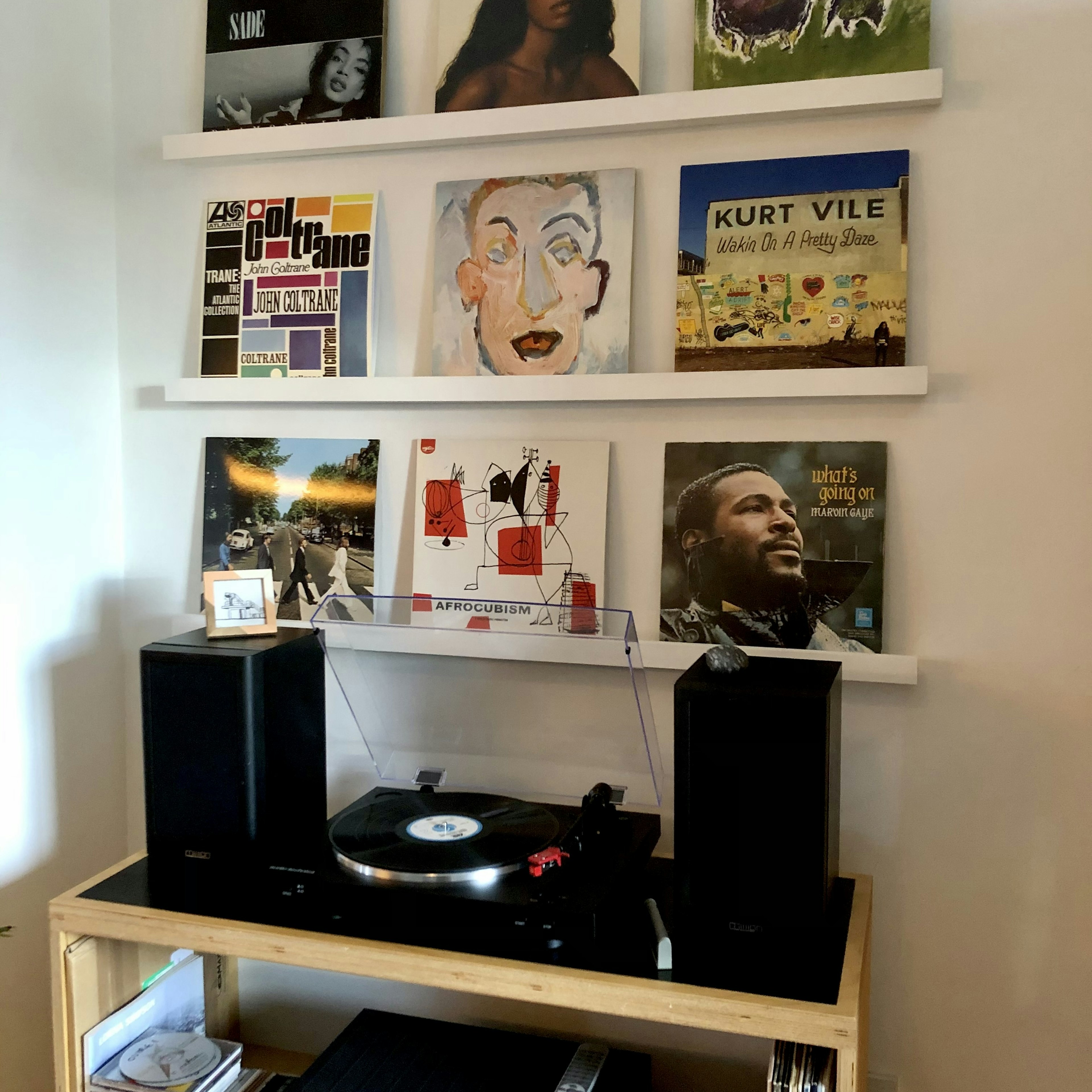A record player and speakers are on a shelf; six albums are displayed on two shelves above.