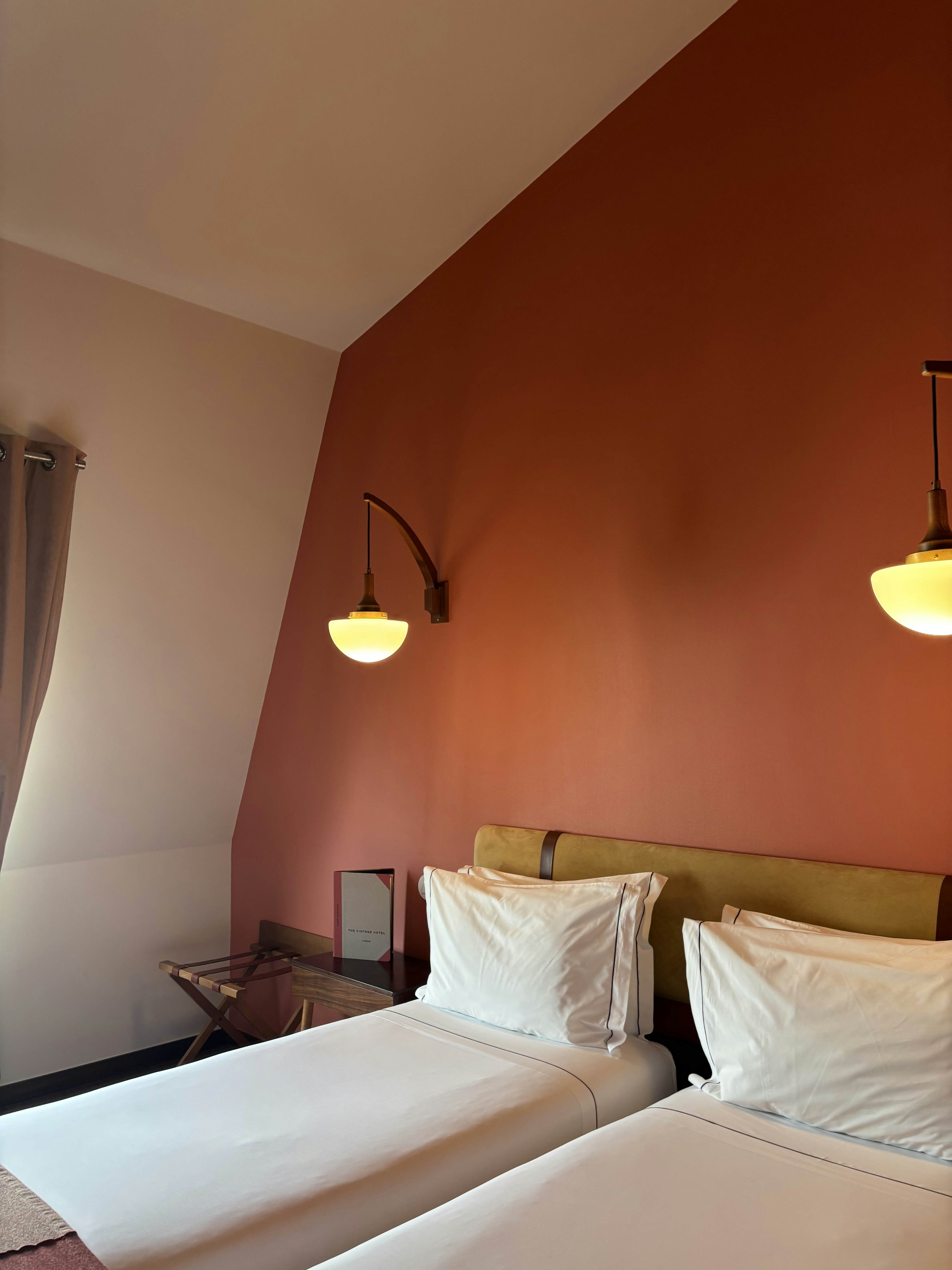 A two-piece bed with a white covering and pillows against a red wall with a lamp sconce.