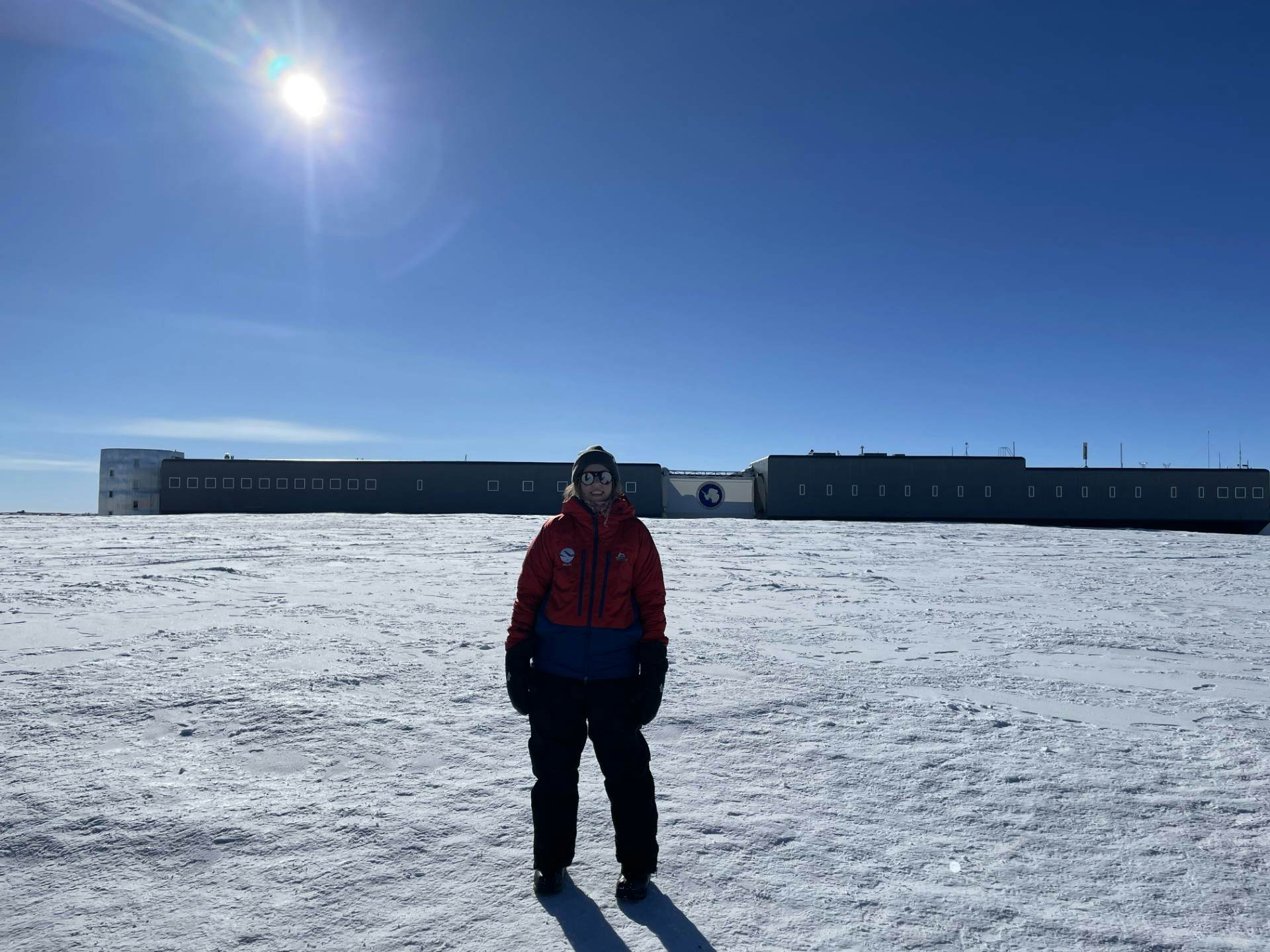 A woman stands in front of a low-rise long building on a snow-covered plateau