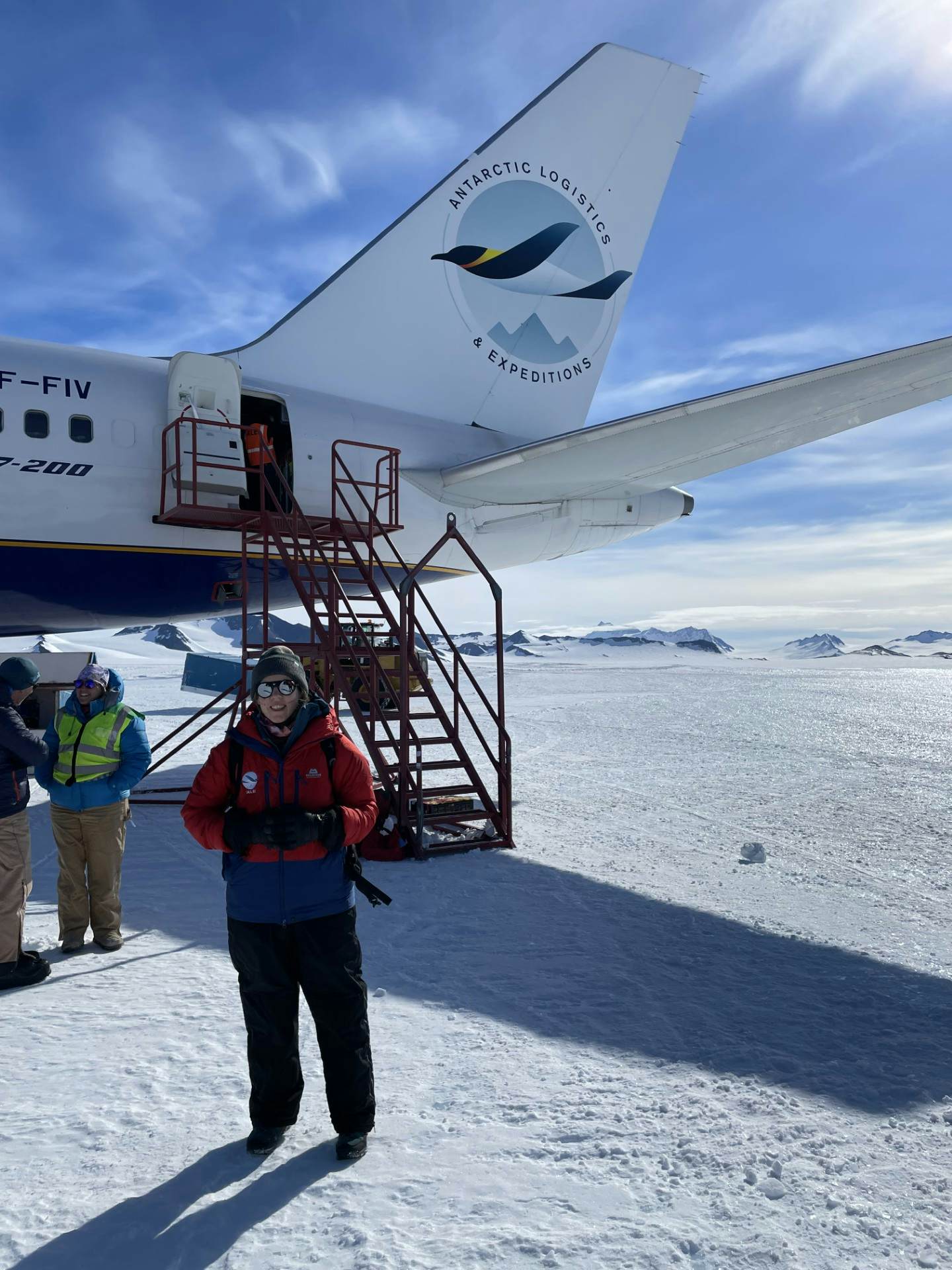 A woman stands in front of the exit stairs from a large commercial airliner on a runway of ice.