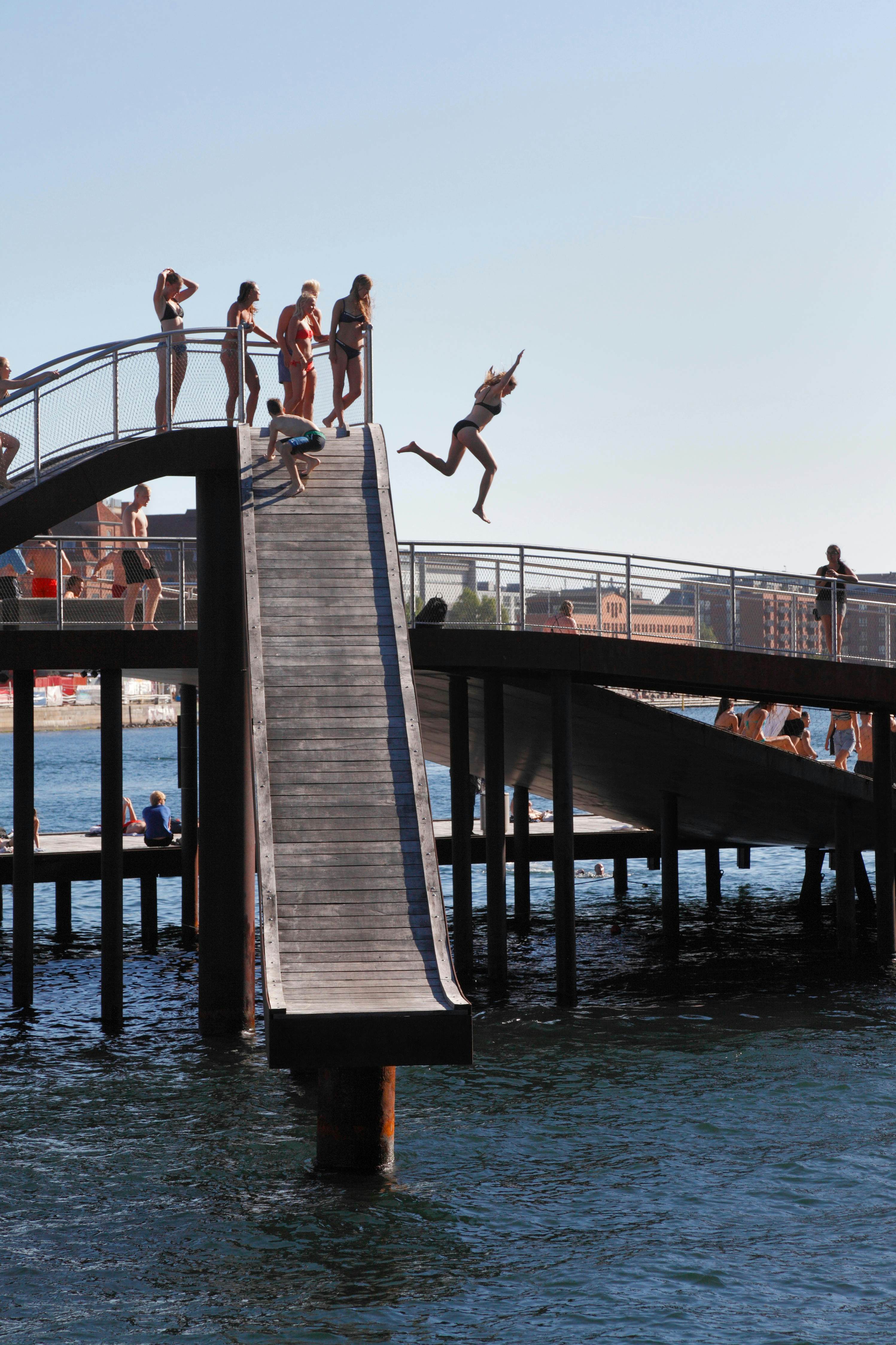 People jump off a structure into water.
