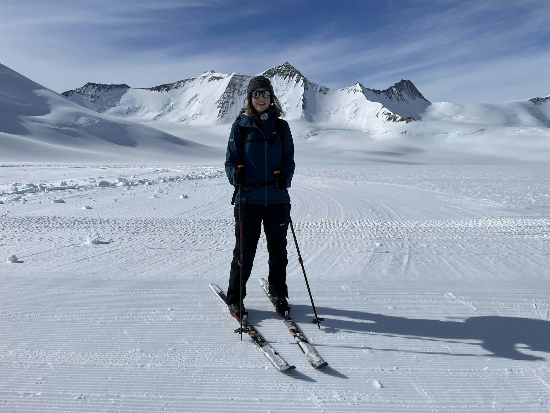 Hikers in deep snow follow a trail downhill through a mountain range.