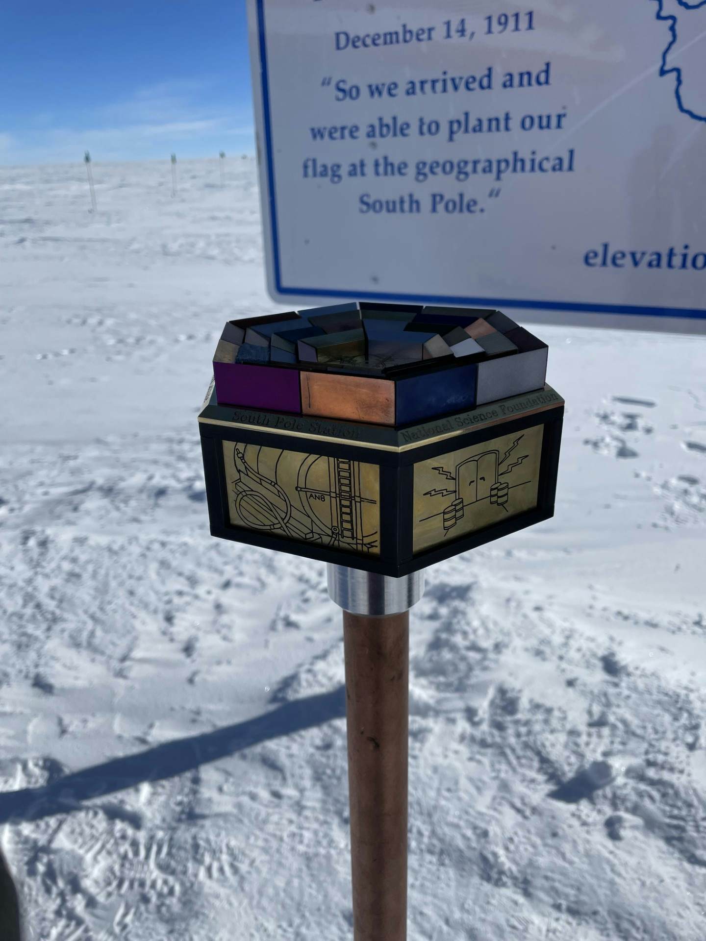 A marker placed in the snow in front of a large sign.