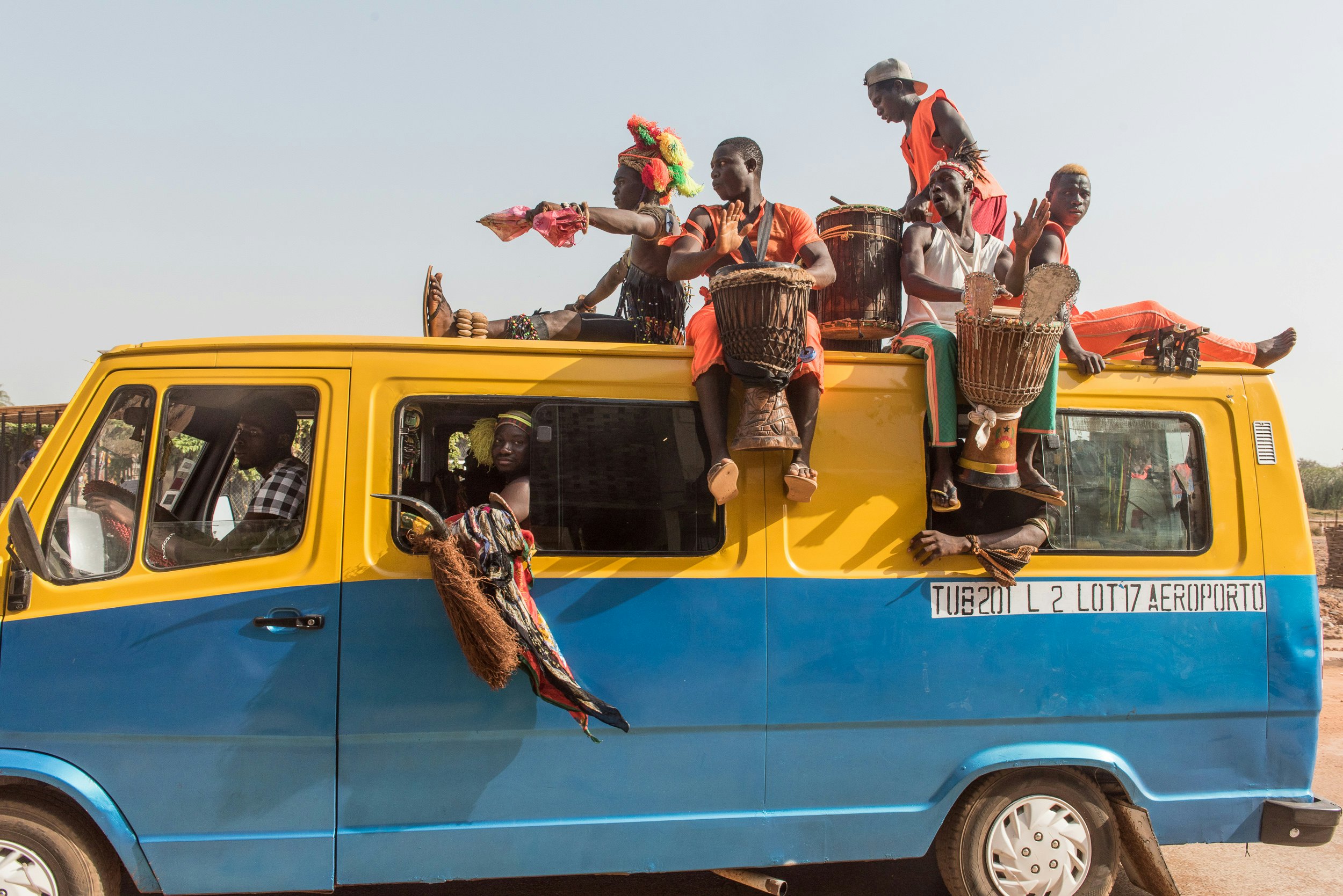 Drummers ride on the top of a blue and yellow van.