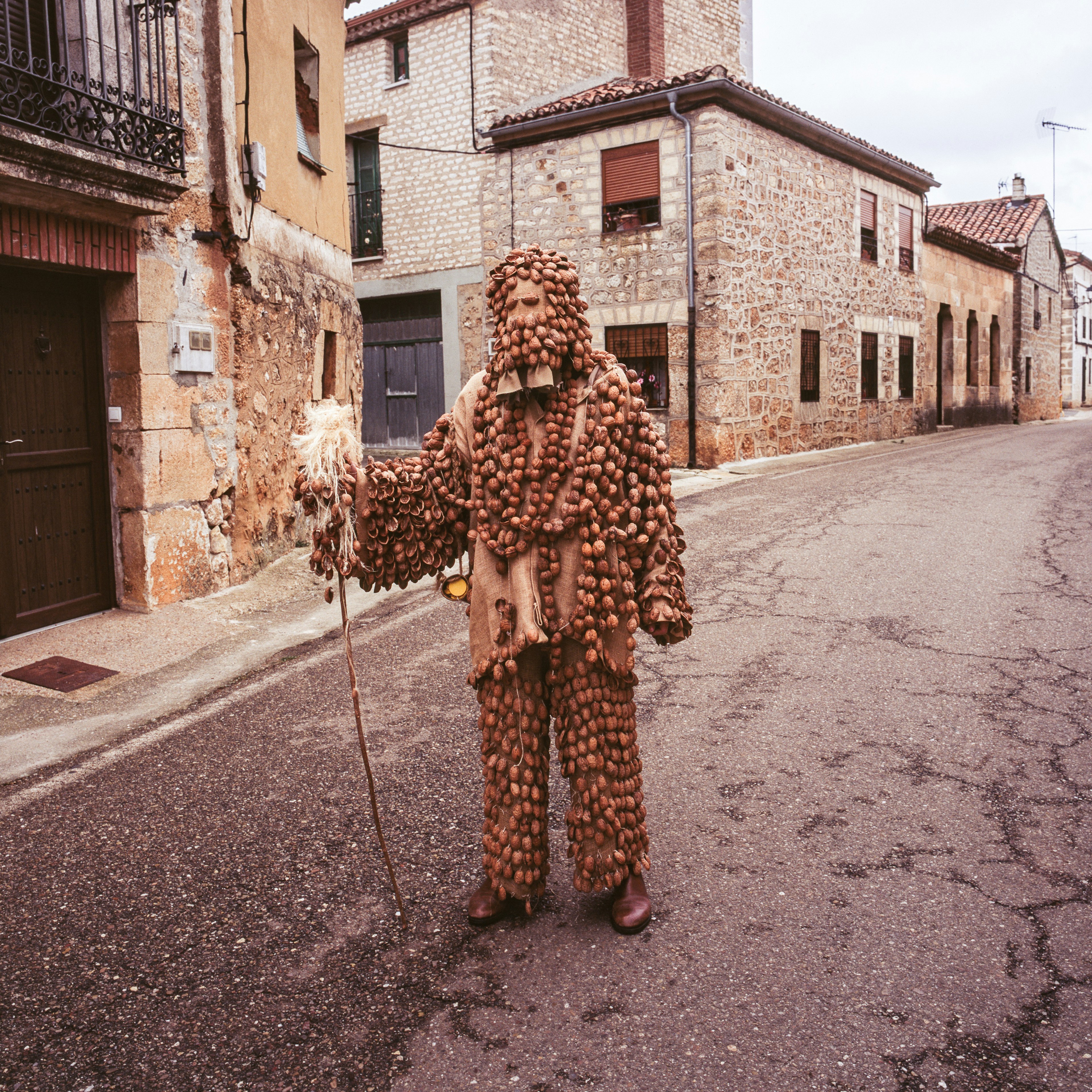 A person wearing a costume made of small round objects stands in an empty street.