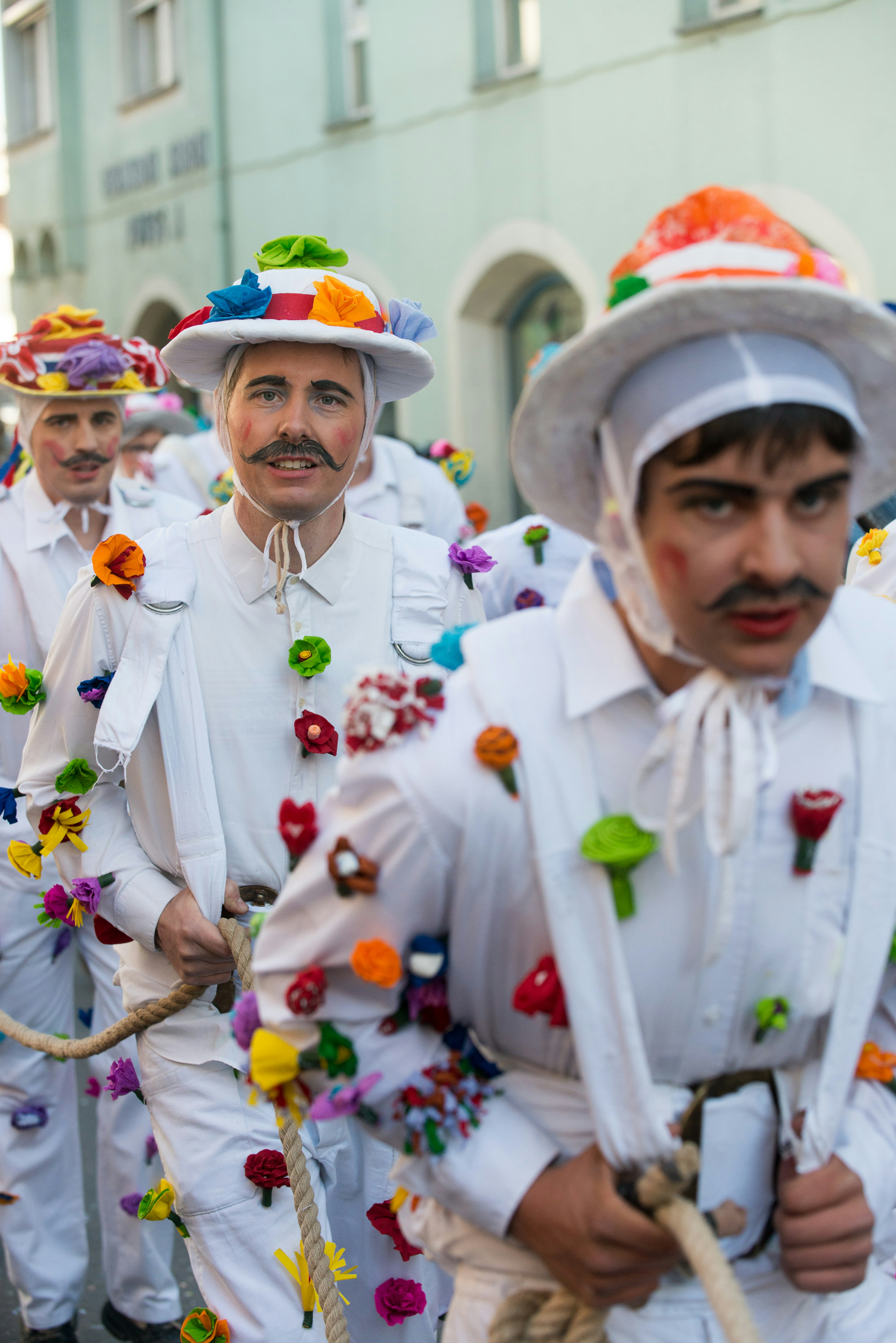 Festival participants wearing white garments strewn with multicolored flowers hold a nautical rope.