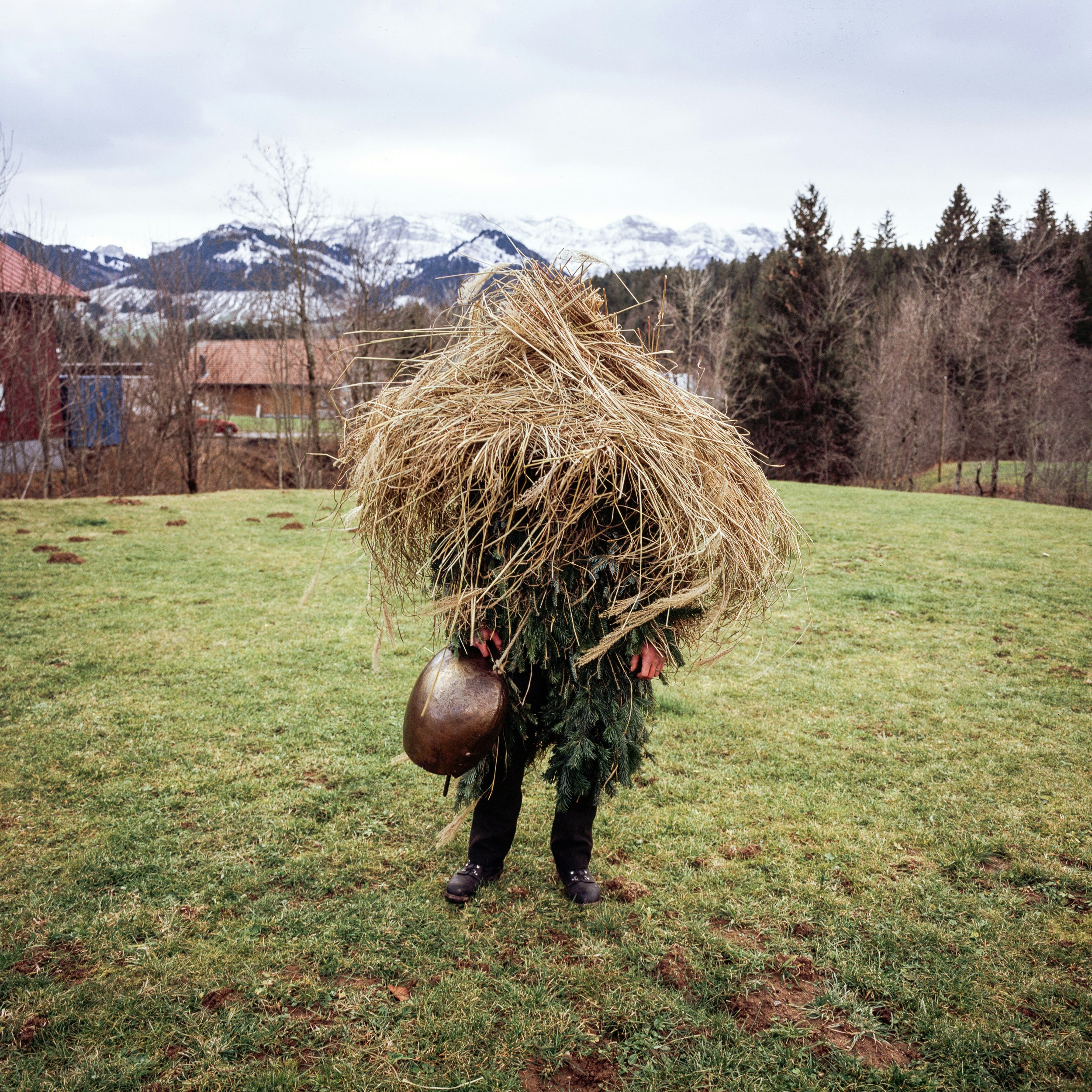 A person wearing a costume made of dried grass and evergreens stands in grass.