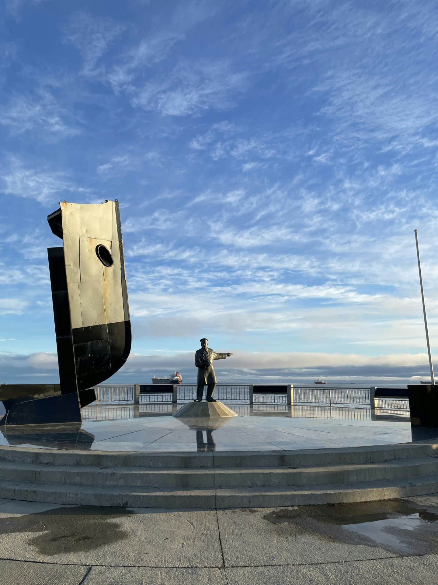 A statue at the edge of the ocean points towards the sea