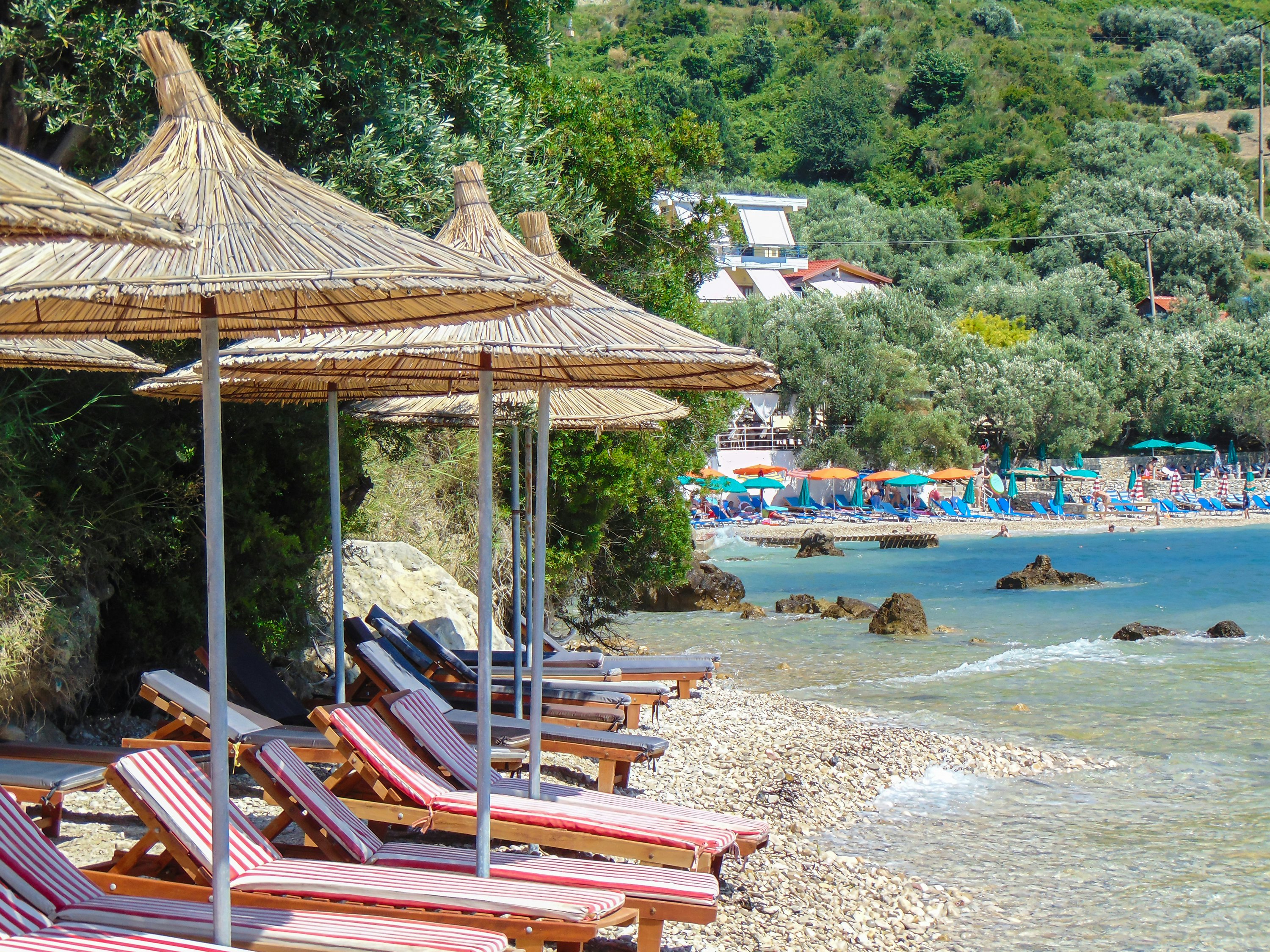 Rocky beach with straw umbrellas and chaise longue, Radhime, Vlore, Albania.